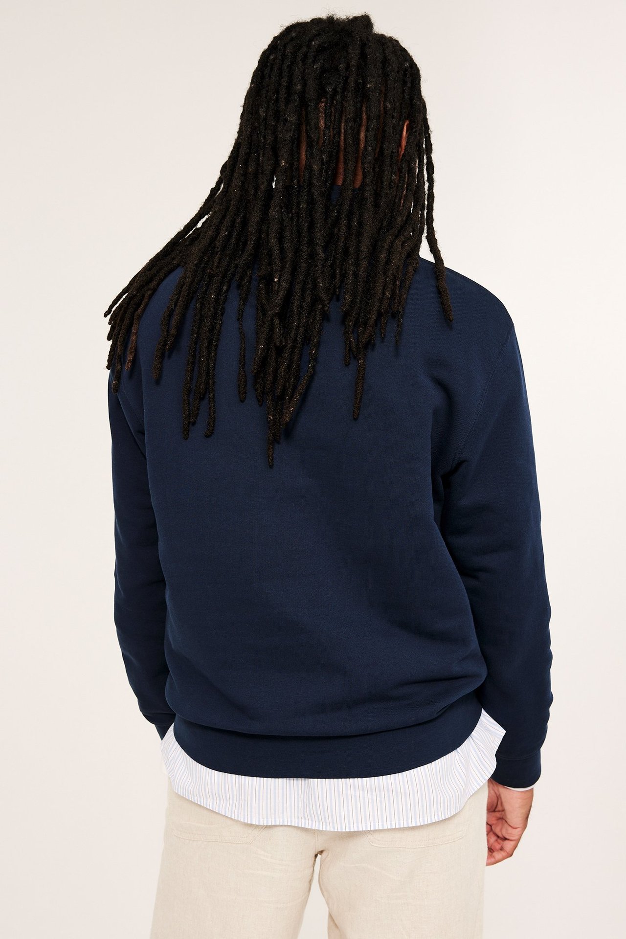 Mężczyzna od tyłu w granatowej bawełnianej bluzie z półzamkiem, na białej koszuli i beżowych spodniach.