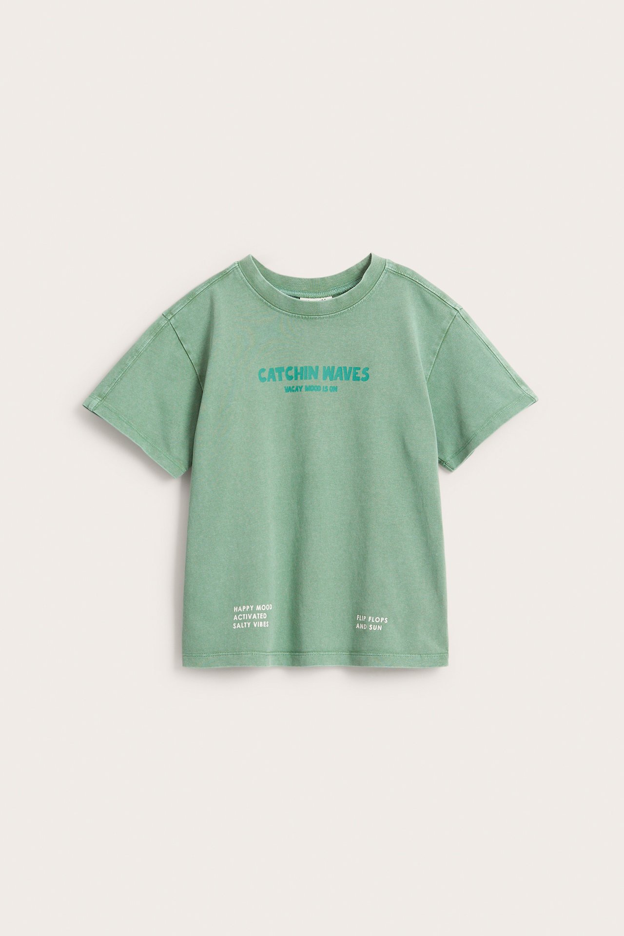 Edestäpäin, vihreä oversize-puuvillapaita, jossa "CATCHIN WAVES" -tekstipainatus edessä.