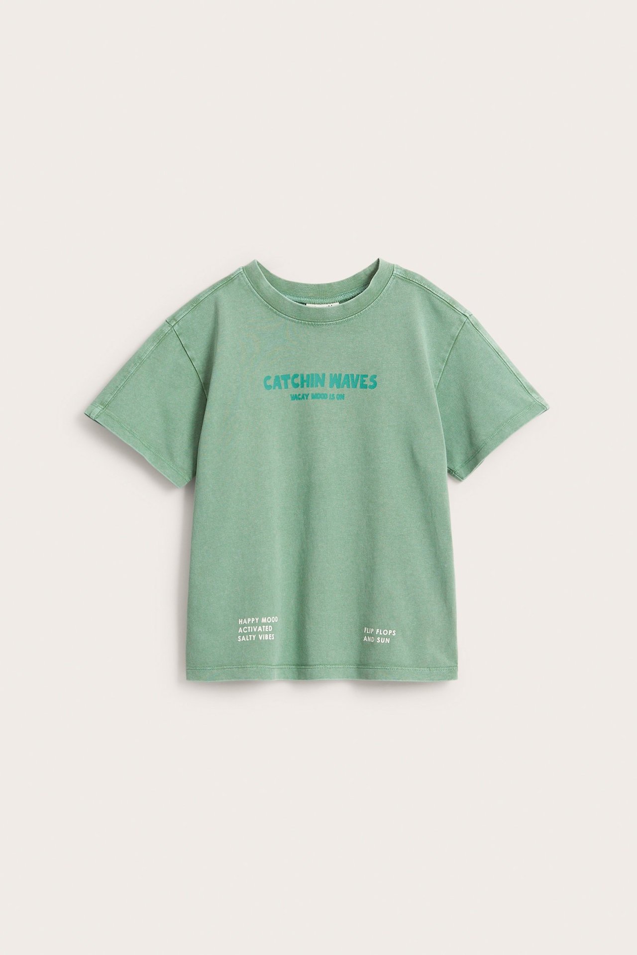 Edestäpäin, vihreä oversize-puuvillapaita, jossa "CATCHIN WAVES" -tekstipainatus edessä.