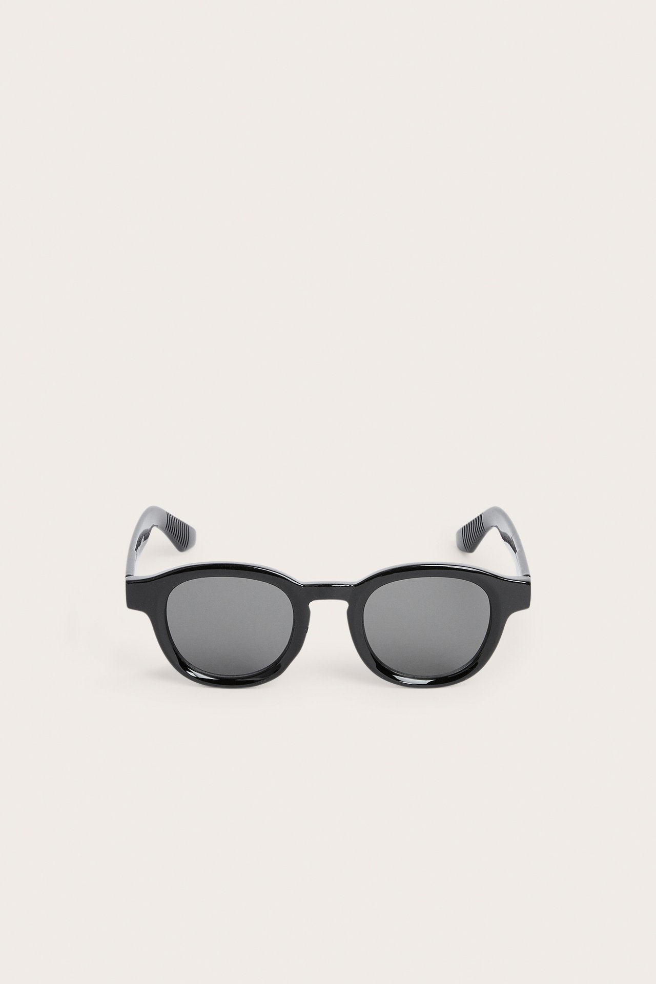 Edestä näkymä mustista pyöreistä muovisista aurinkolaseista tummilla linsseillä.