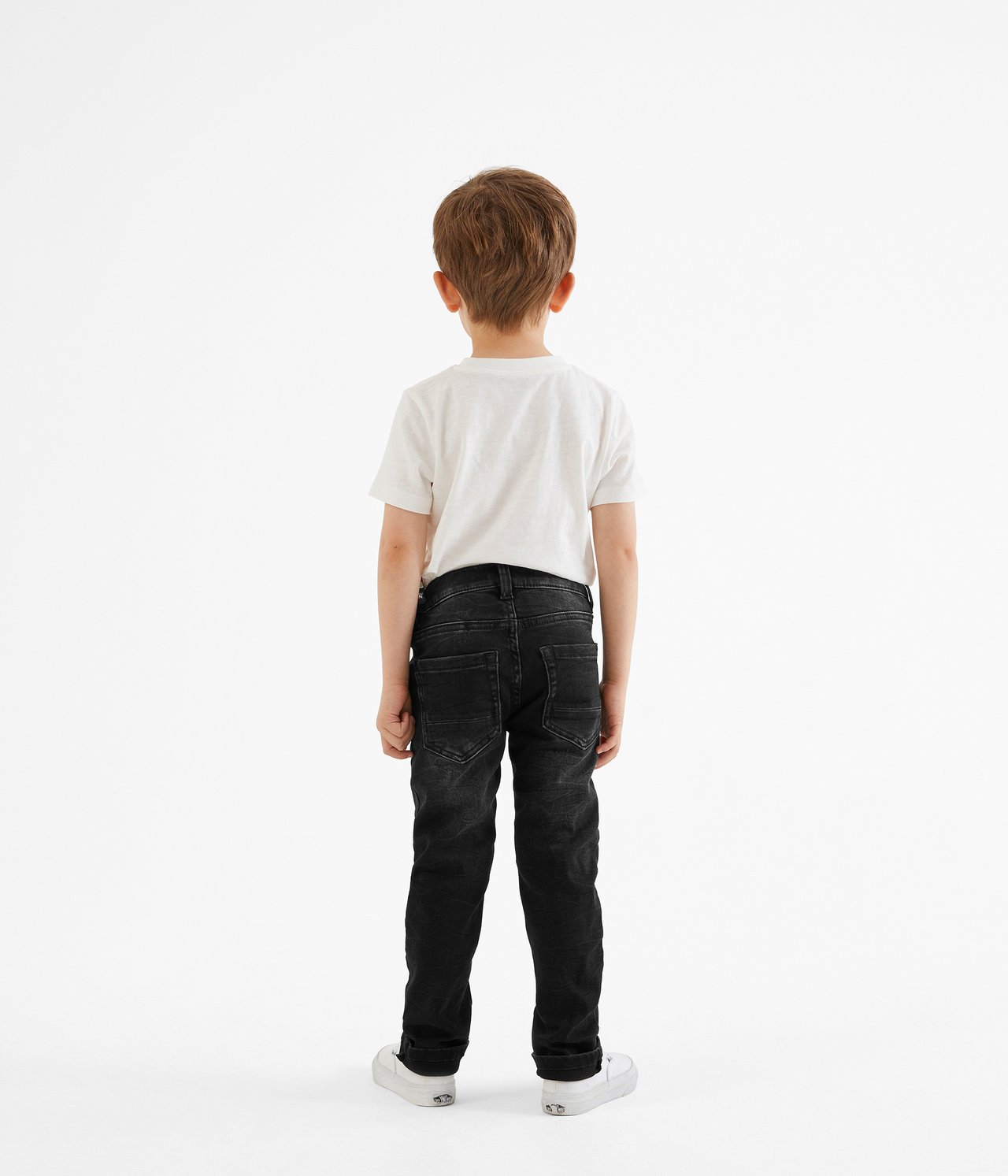 Bakifrån, ett barn i svarta slim-fit joggerjeans, vit t-shirt och vita sneakers.