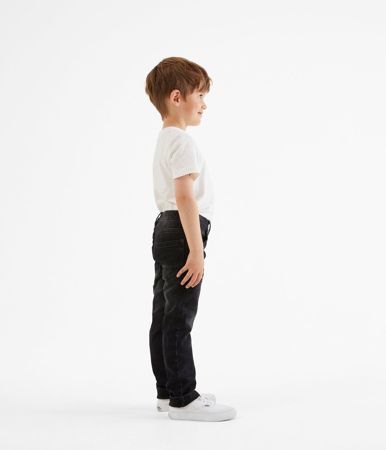 Sidovy av ett barn i svarta slim-fit joggerjeans, en vit t-shirt och vita sneakers.