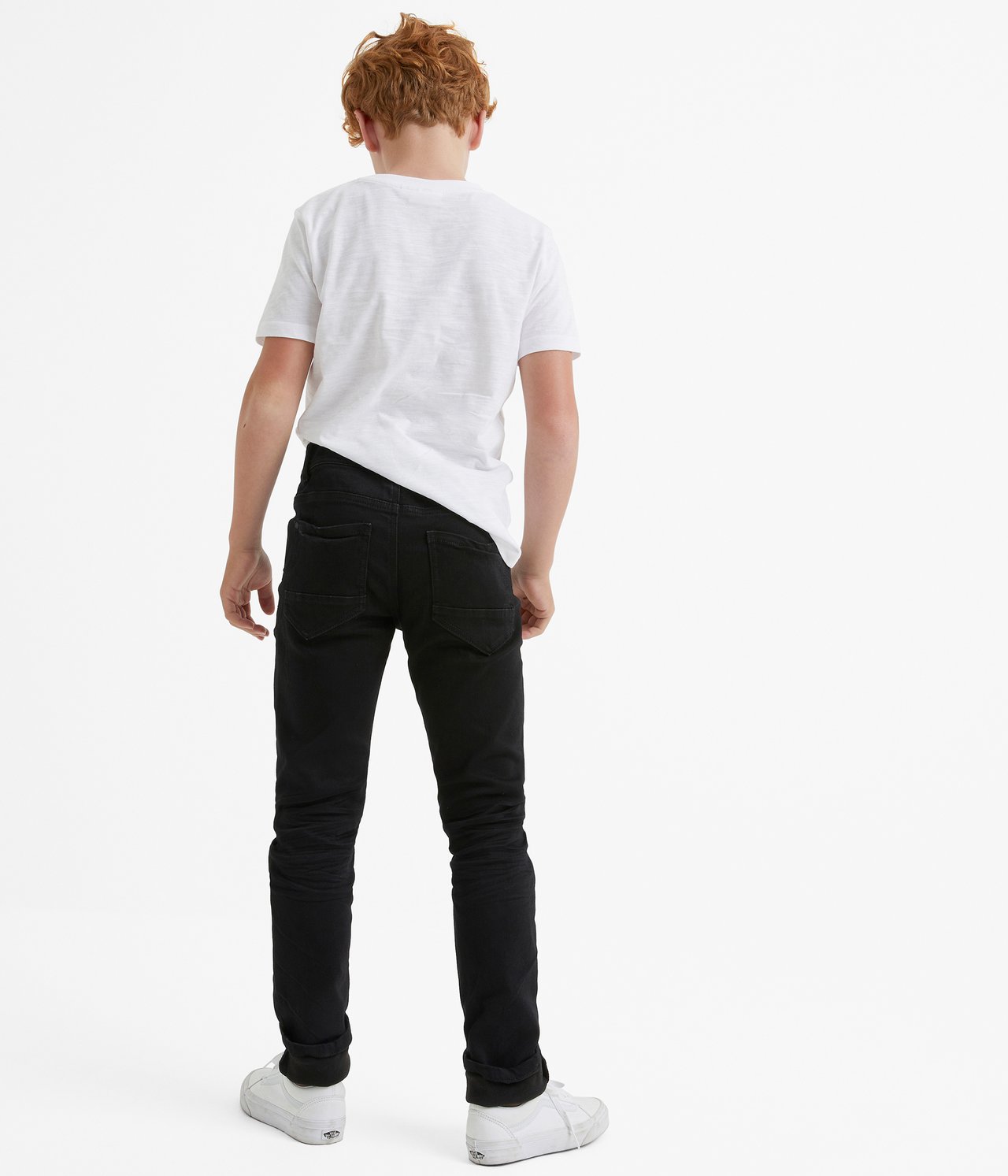 Widok z tyłu dziecka w czarnych dżinsach jogger slim-fit, białej koszulce i białych trampkach.