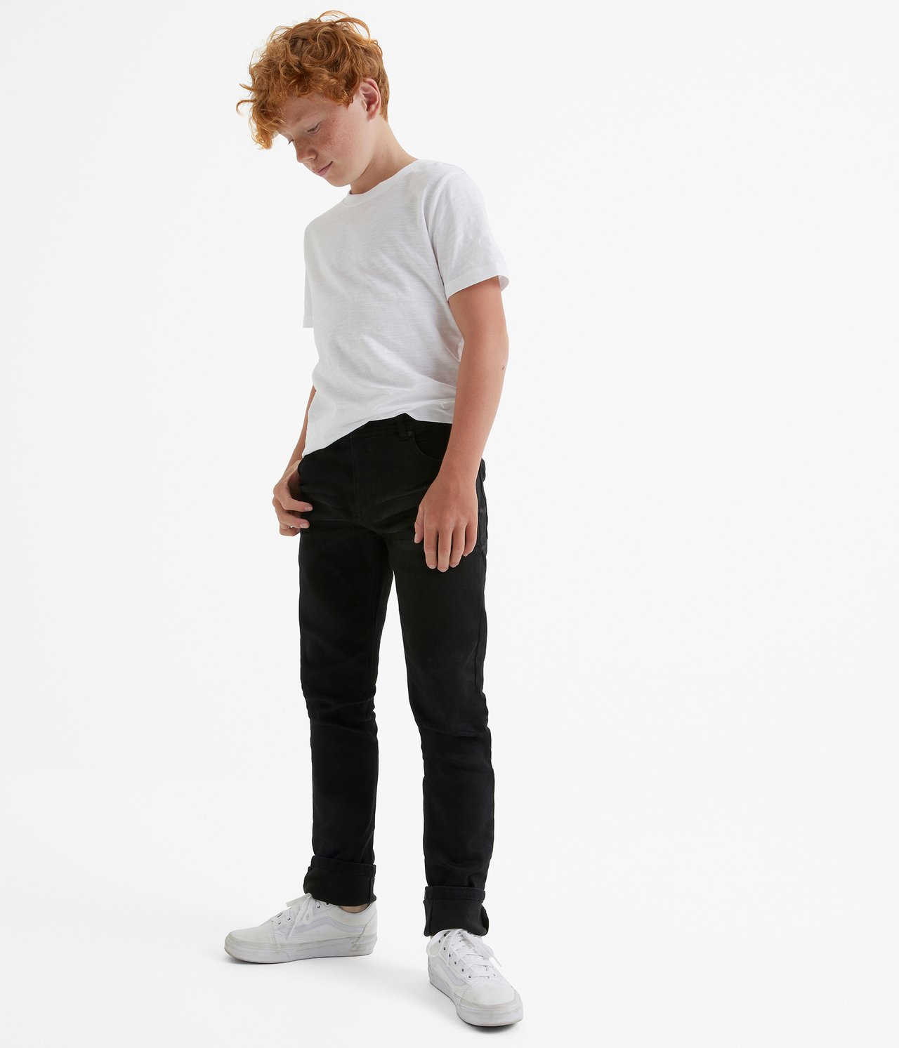 Widok z przodu dziecka w czarnych dżinsach jogger slim fit, białym T-shircie i białych trampkach.