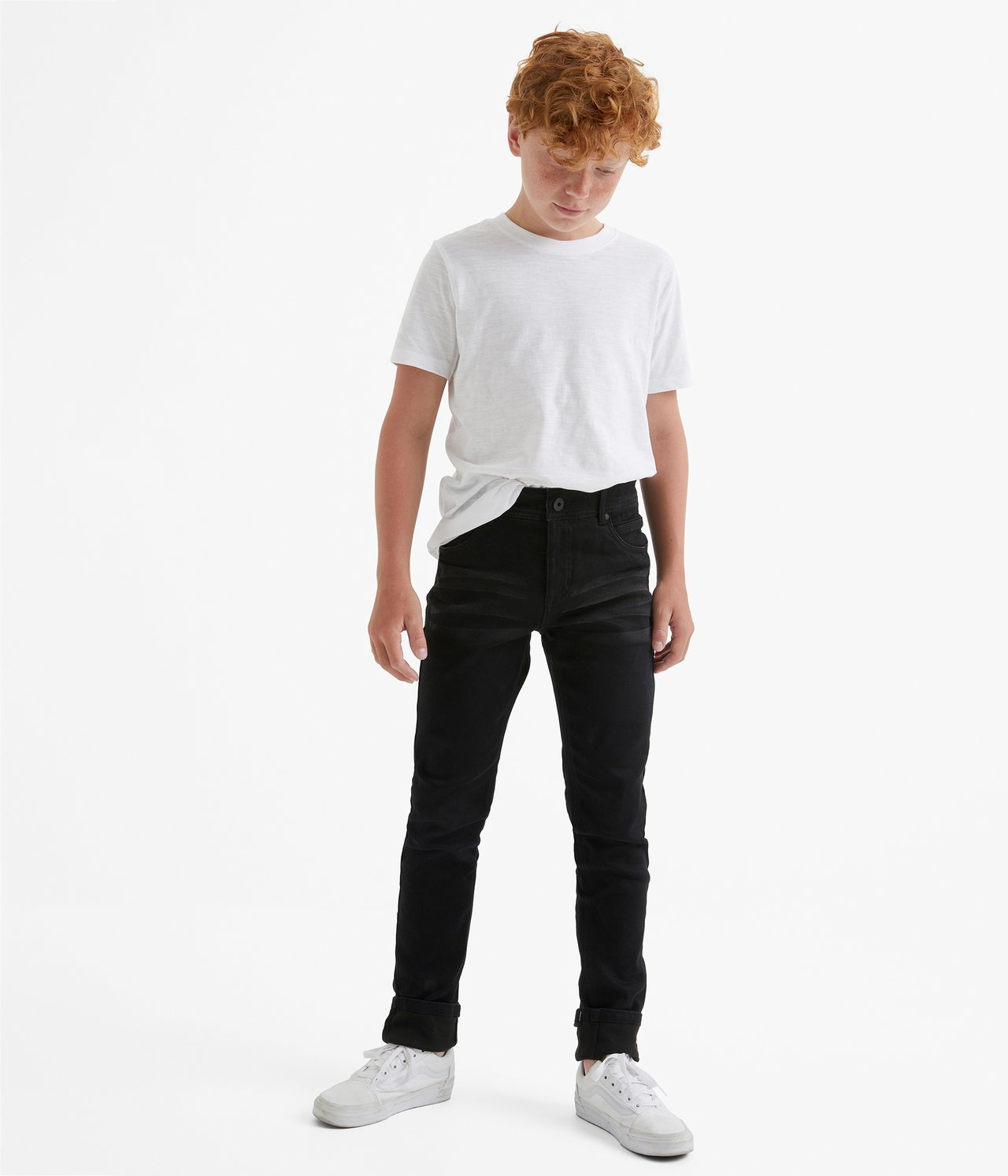 Widok z przodu dziecka w czarnych dżinsach jogger slim fit, białym t-shircie i białych trampkach.