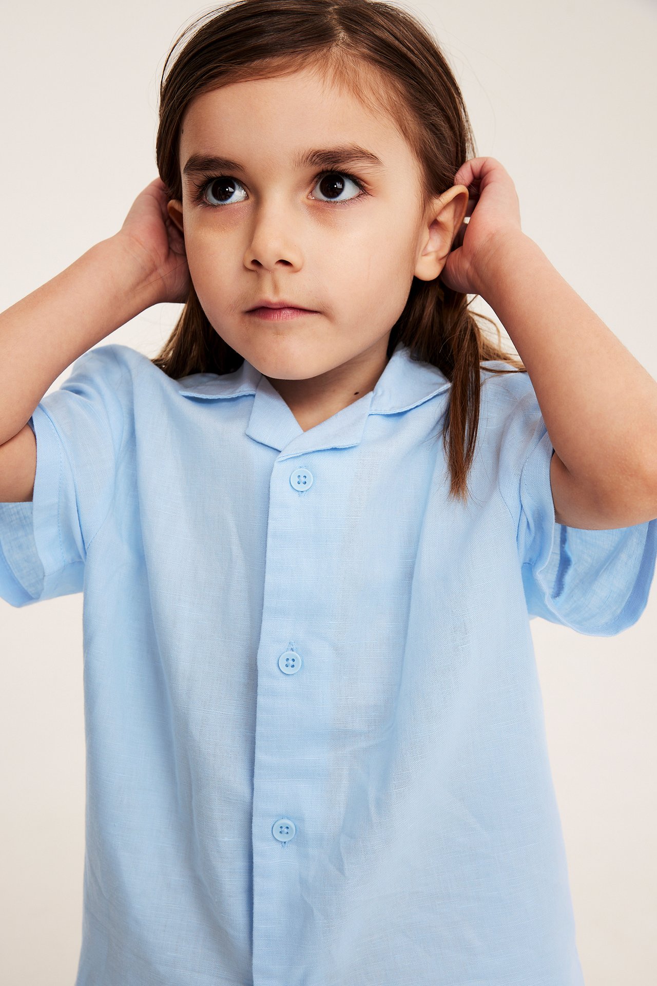 Edestäpäin lapsi, jolla on vaaleansininen pellavasekoite lyhythihainen resort-paita napeilla.