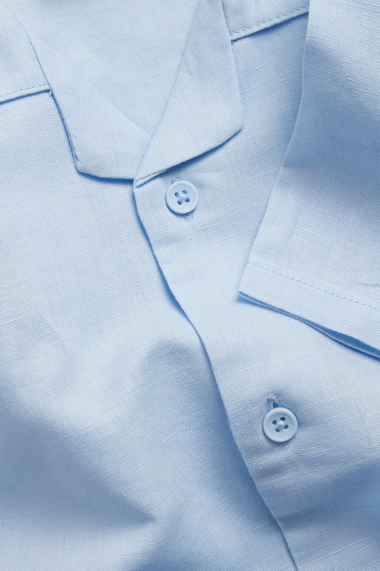 Lähikuva vaaleansinisestä pellavasekoitteisesta lyhythihaisesta paitapuserosta, jossa on kaulus ja napit.