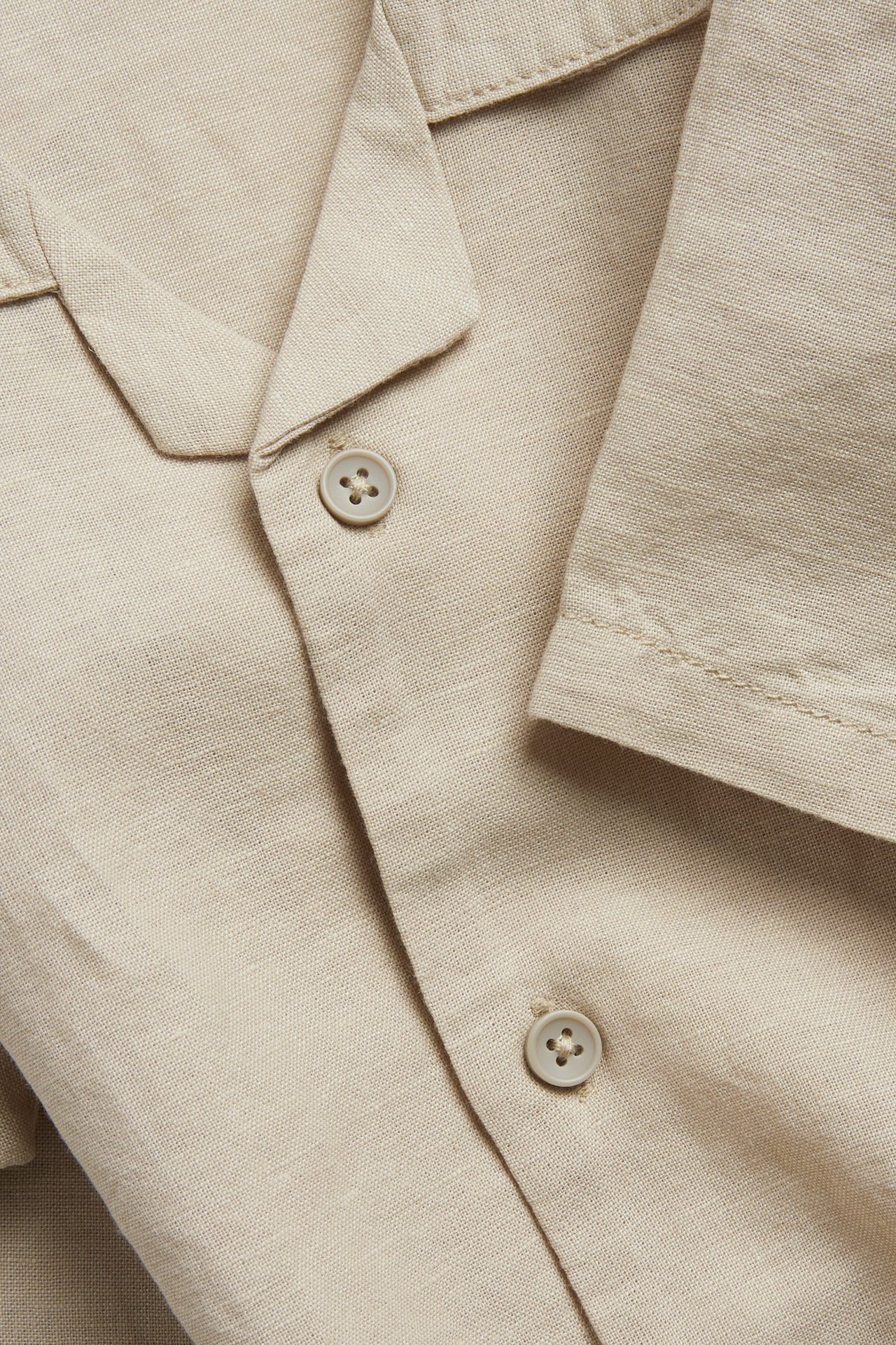 Lähikuva beigestä pellavasekoitteisesta lyhythihaisesta paitasta, jossa on resort-kaulus ja napit edessä.