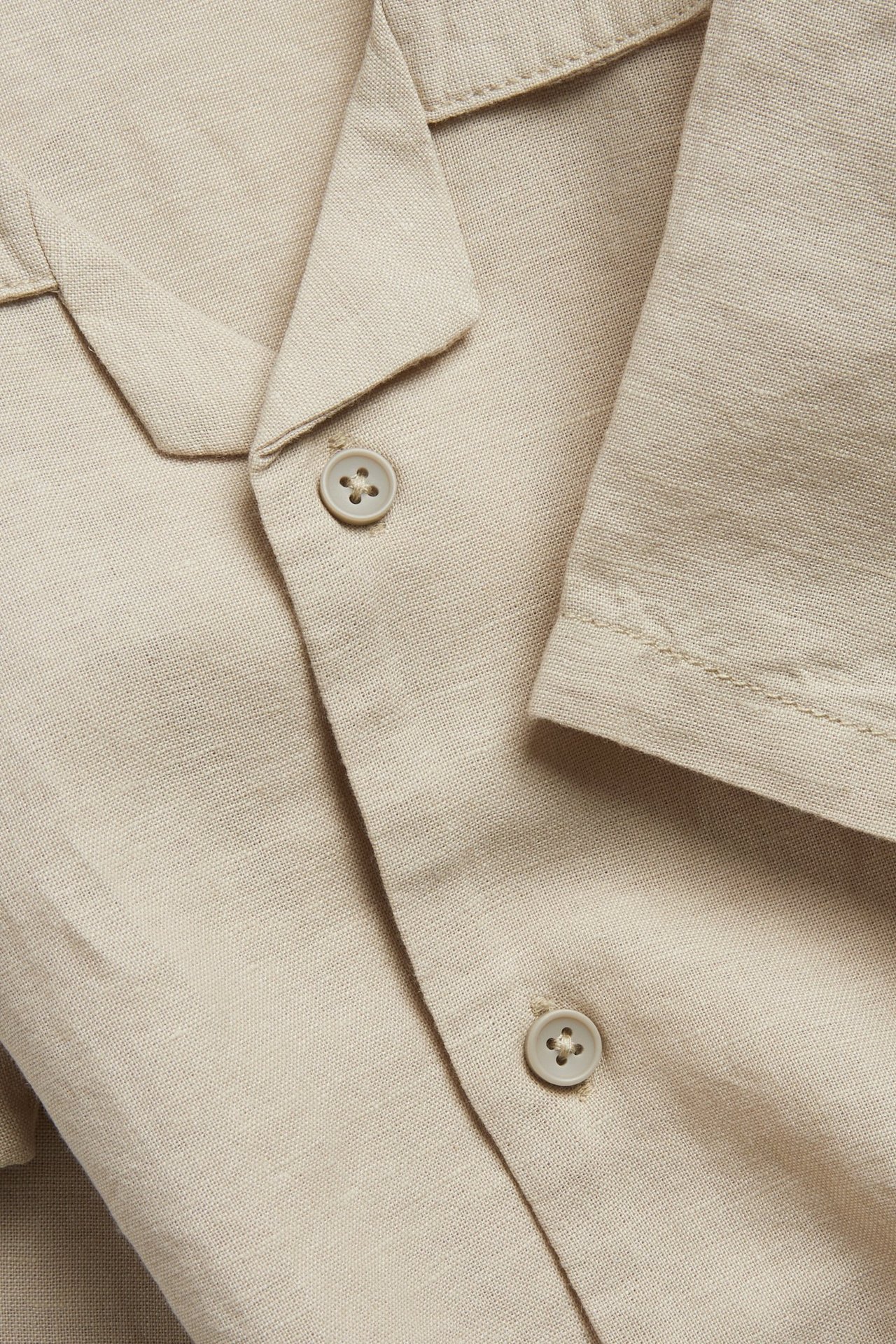 Närbild av en beige kortärmad skjorta i linneblandning med resortkrage och knappar fram.