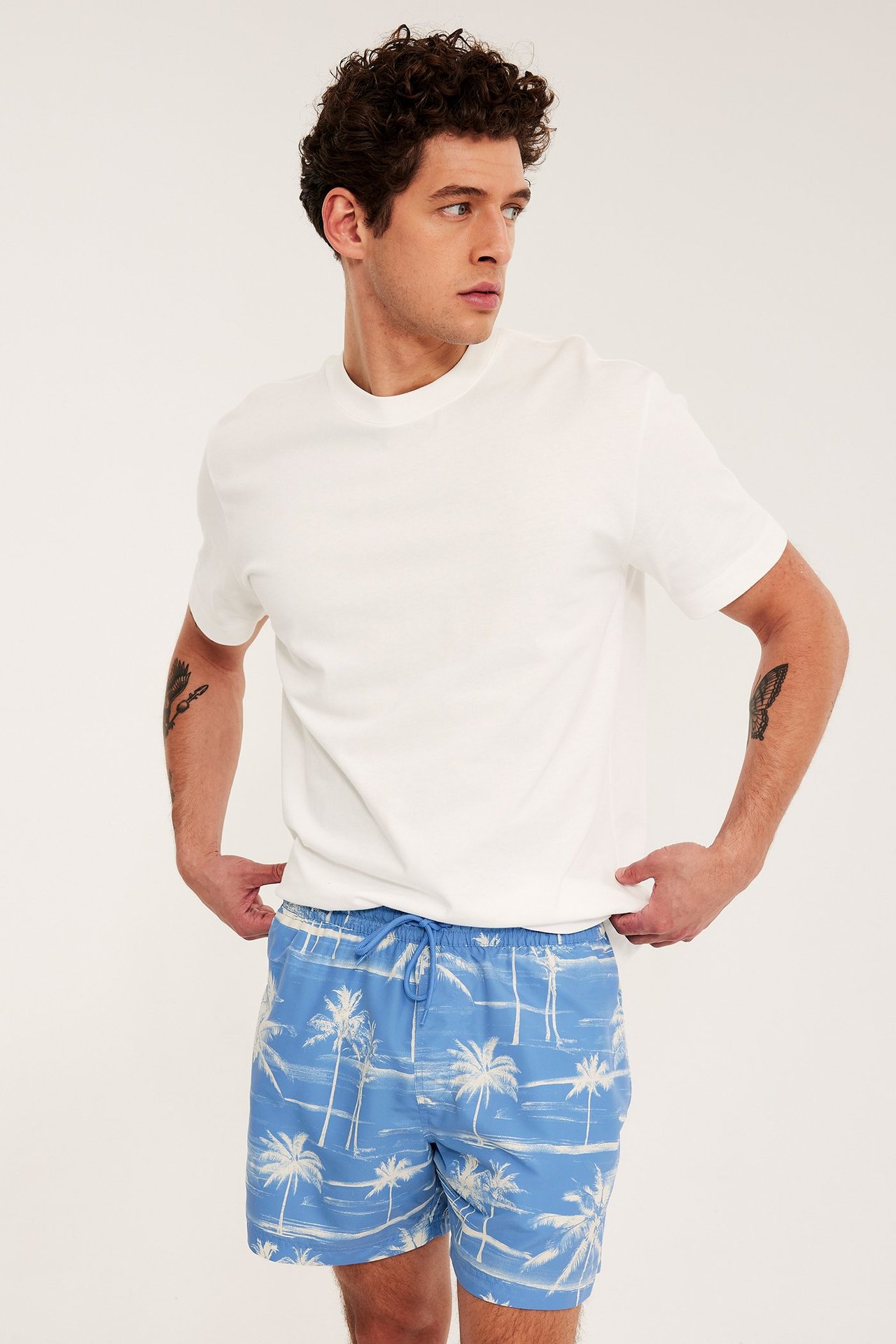 Frontvy av en man i ljusblå mönstrade badshorts med dragsko i midjan och en vit t-shirt.