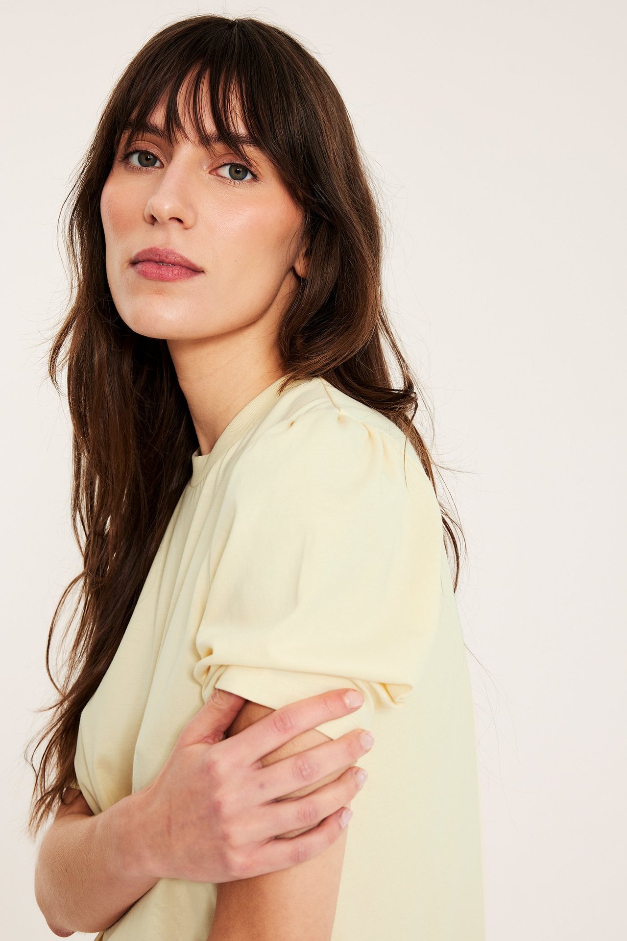 Nærbilde av en kvinne i en lys gul bomullstopp med korte puffermer, sett fra siden.