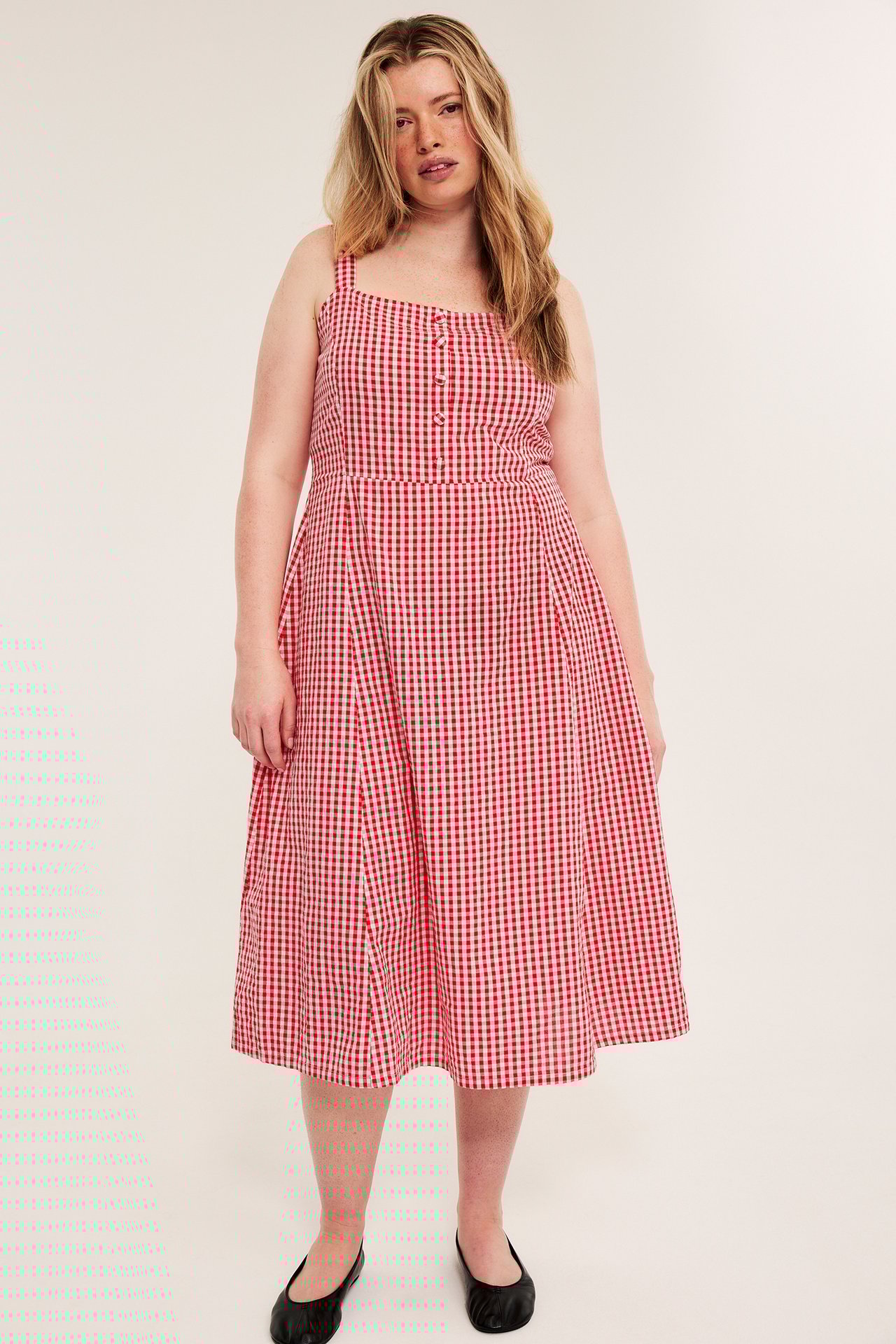 Kvinne i rød- og hvitrutet midikjole i bomull med stofftrukne knapper og svarte ballerinasko.