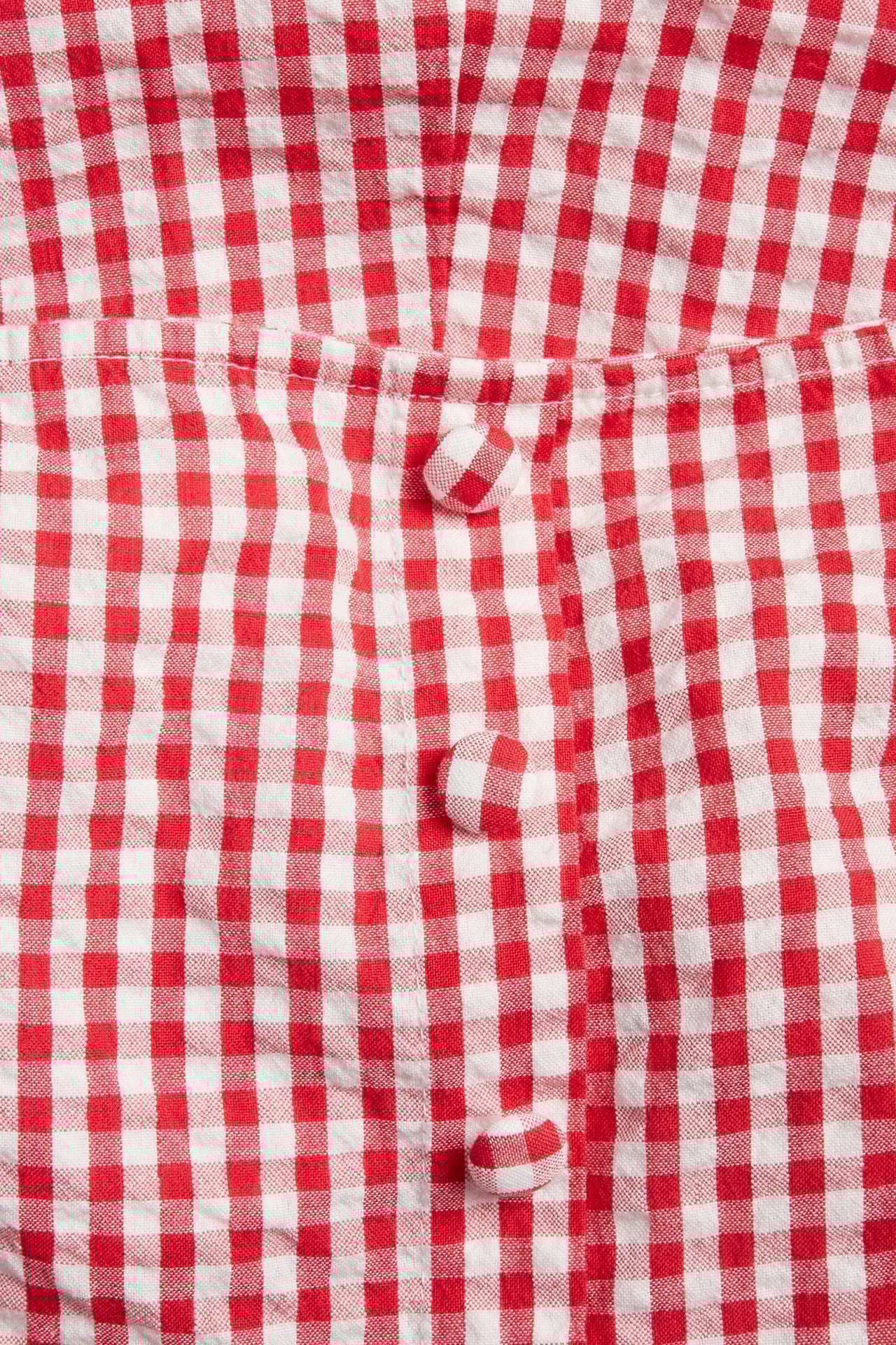 Närbild på en röd- och vitrutig bäckebölja-klänning med matchande klädda knappar.