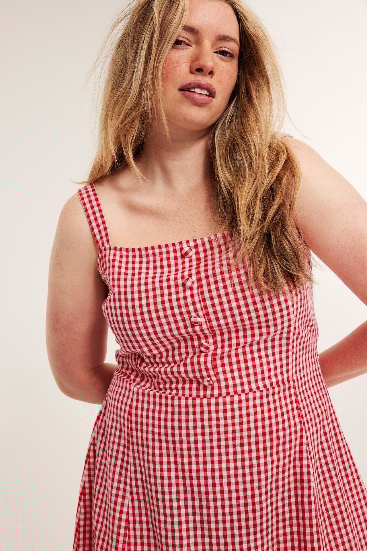 Frontbilde av en kvinne i rød- og hvitrutet bomullskjole i seersucker med stofftrukne knapper.