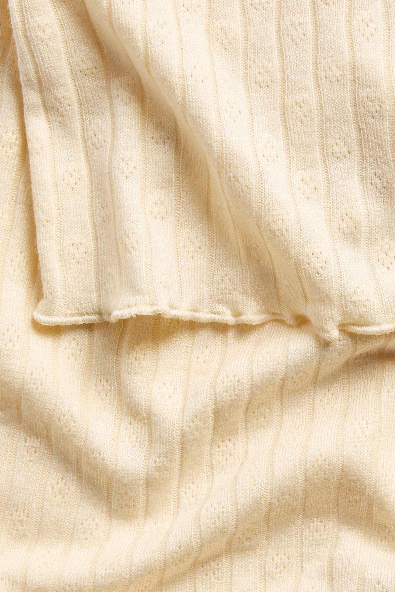 Nærbilde av en lys gul pointelle strikket topp med vertikal ribbet tekstur.