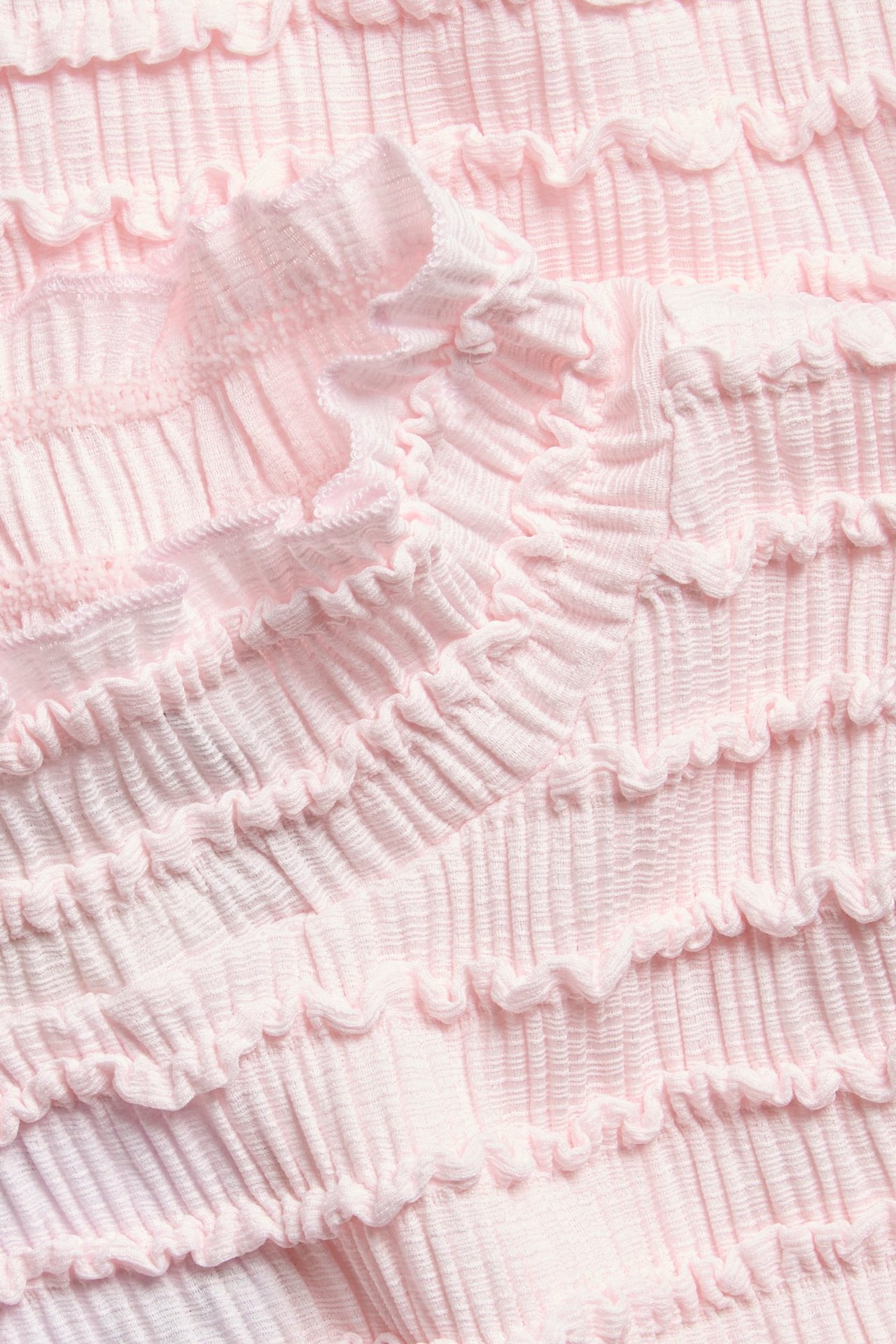 Zbliżenie jasnoróżowego topu z poziomymi falbankami i detalami babylock.