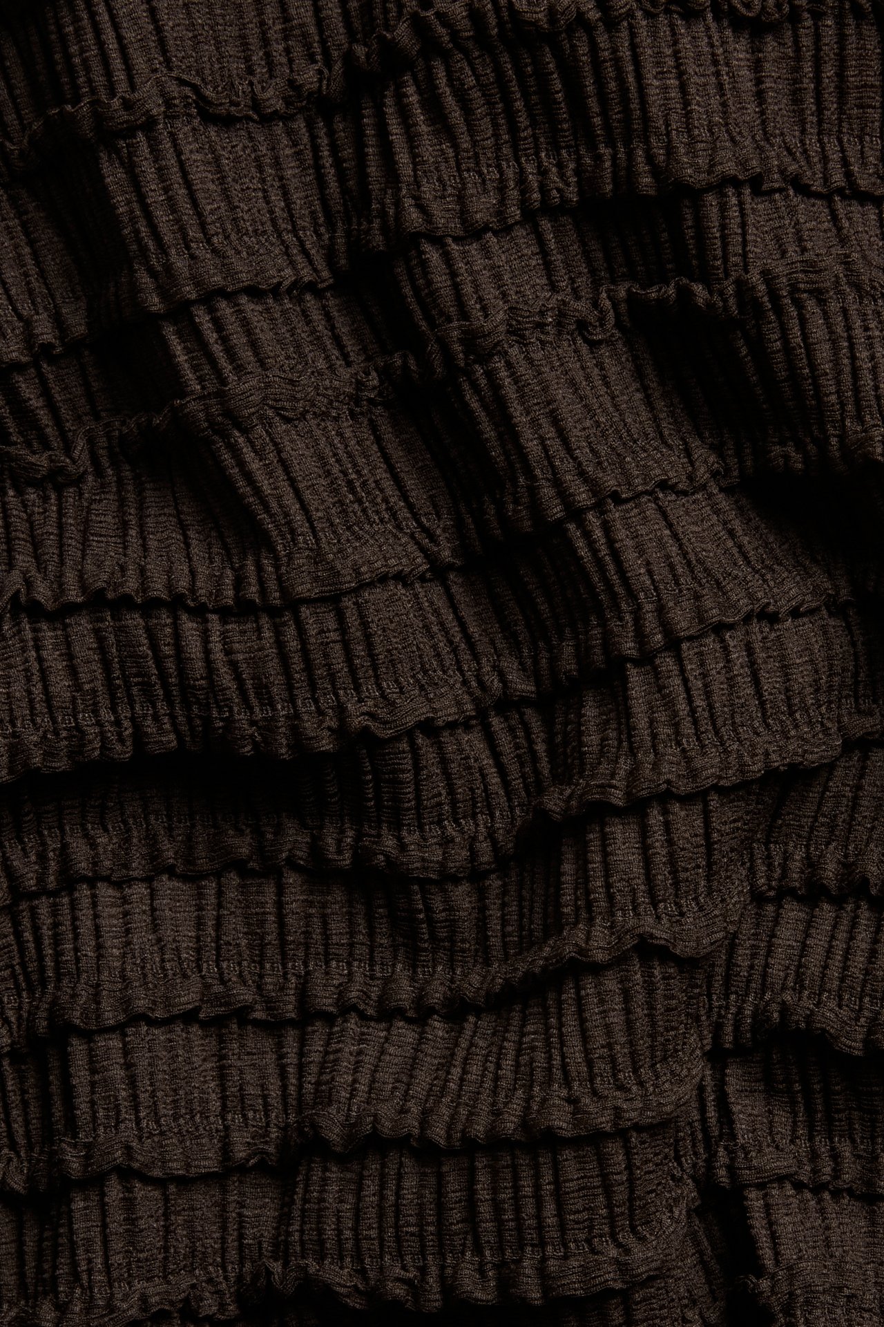 Lähikuva tummanruskeasta strukturoidusta topin kankaasta, jossa on poimutettu pinta.