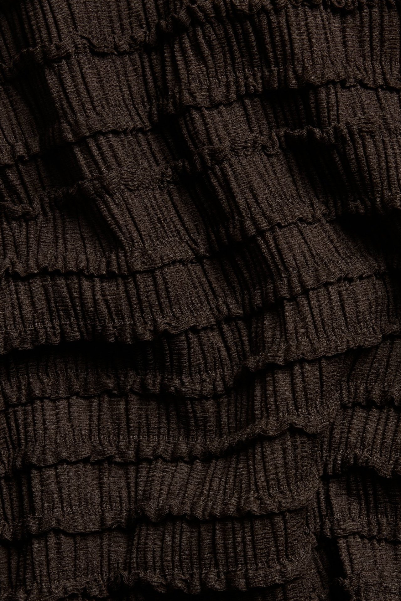 Zbliżenie na ciemnobrązową, strukturalną tkaninę topu z marszczoną powierzchnią.