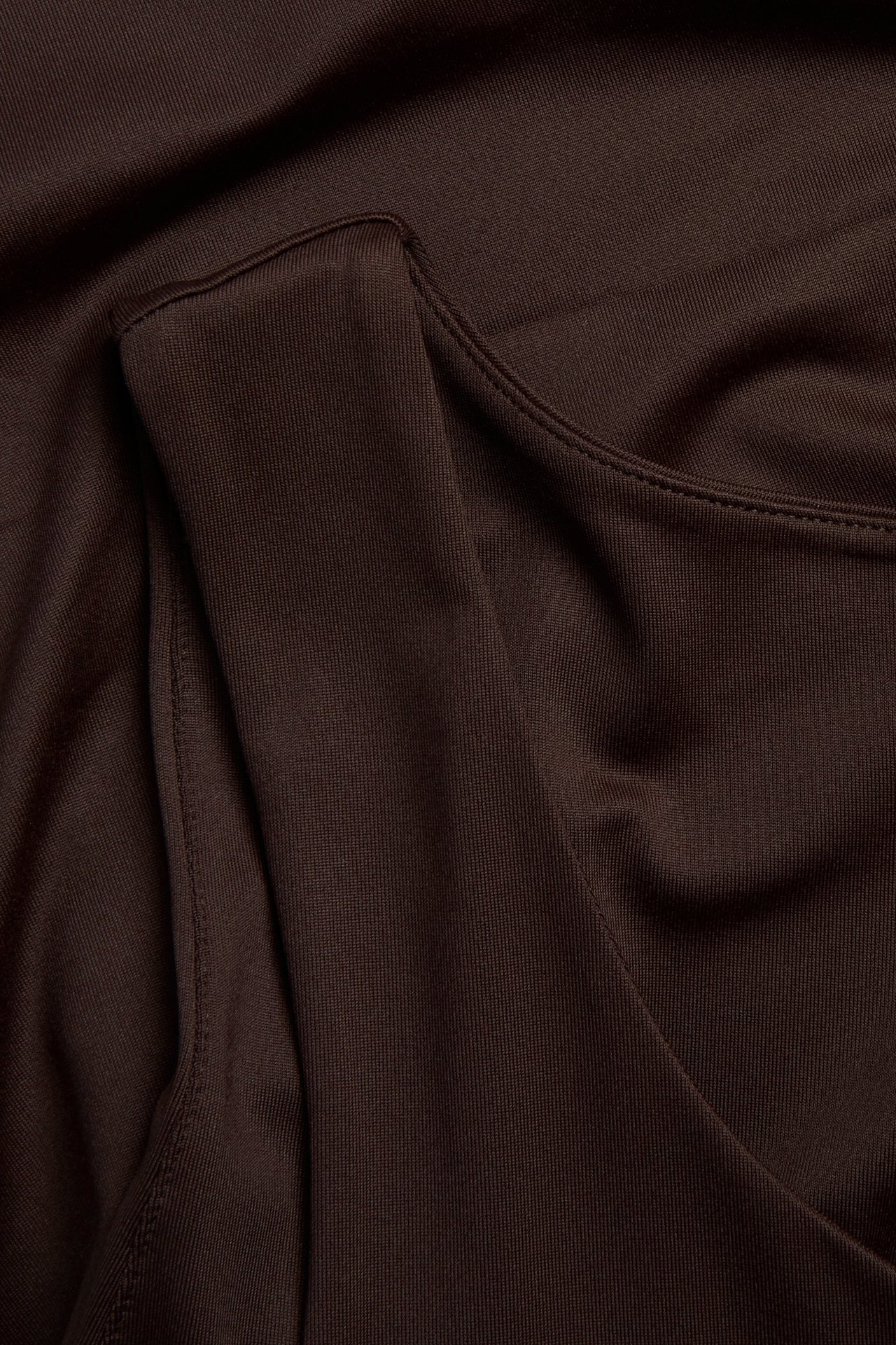Lähikuva tummanruskeasta, vartalonmyötäisestä topista sileästä, joustavasta kankaasta näkyvillä ompeleilla.