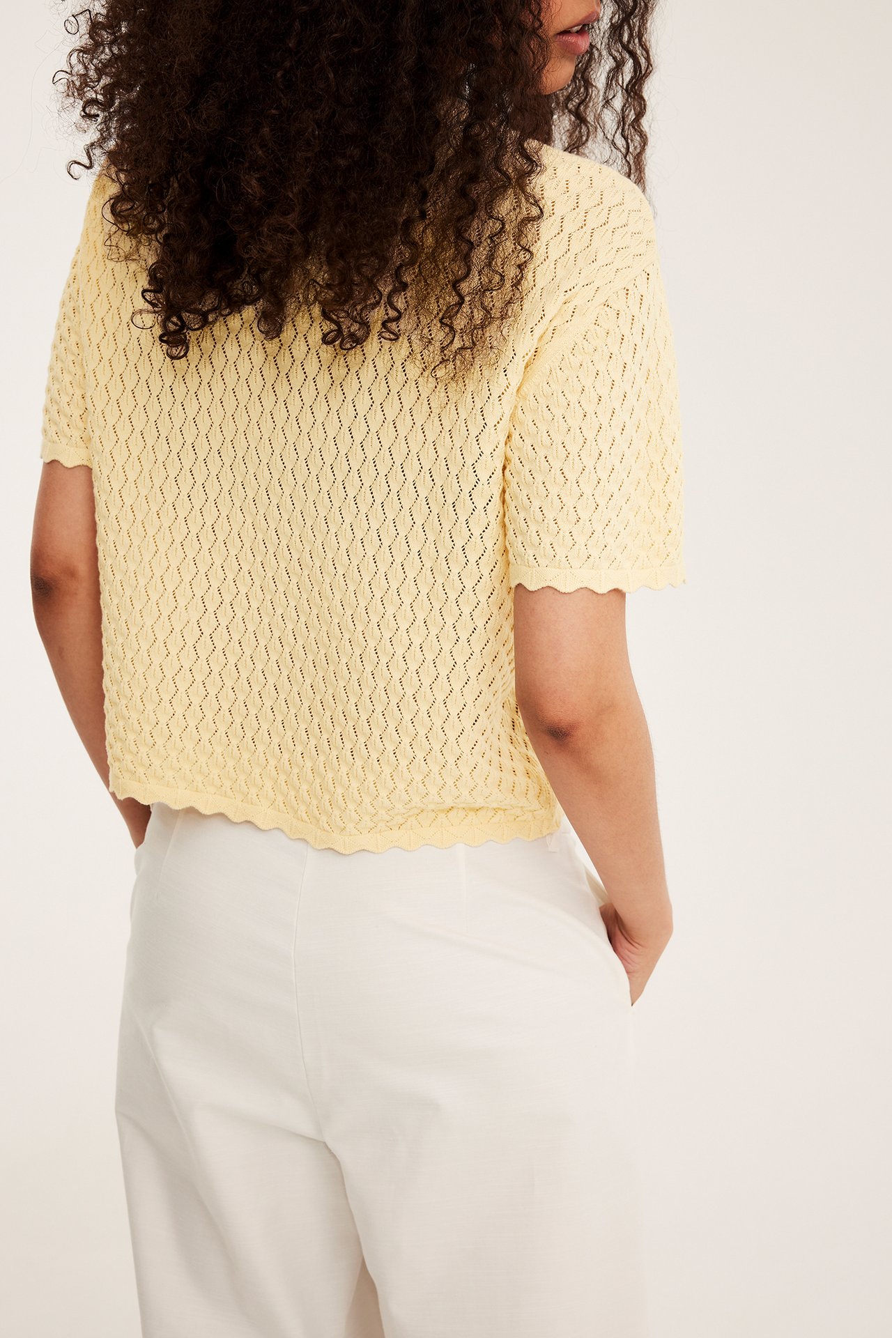 Bakfra: kvinne i lys gul mønsterstrikket kortermet genser og lyse bukser.