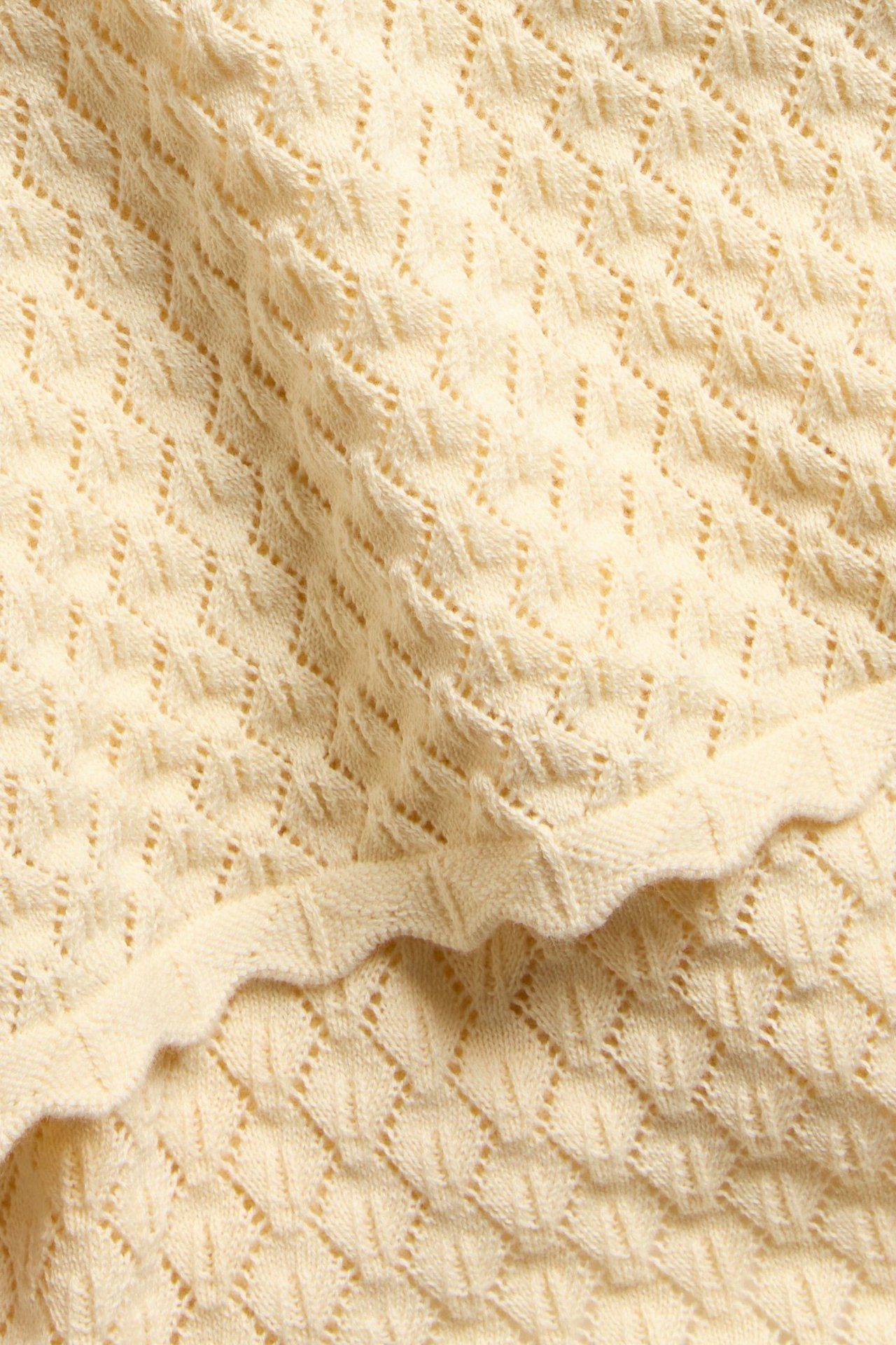Zbliżenie na jasnożółty bawełniany sweter z krótkim rękawem, wzorem i falistym brzegiem.