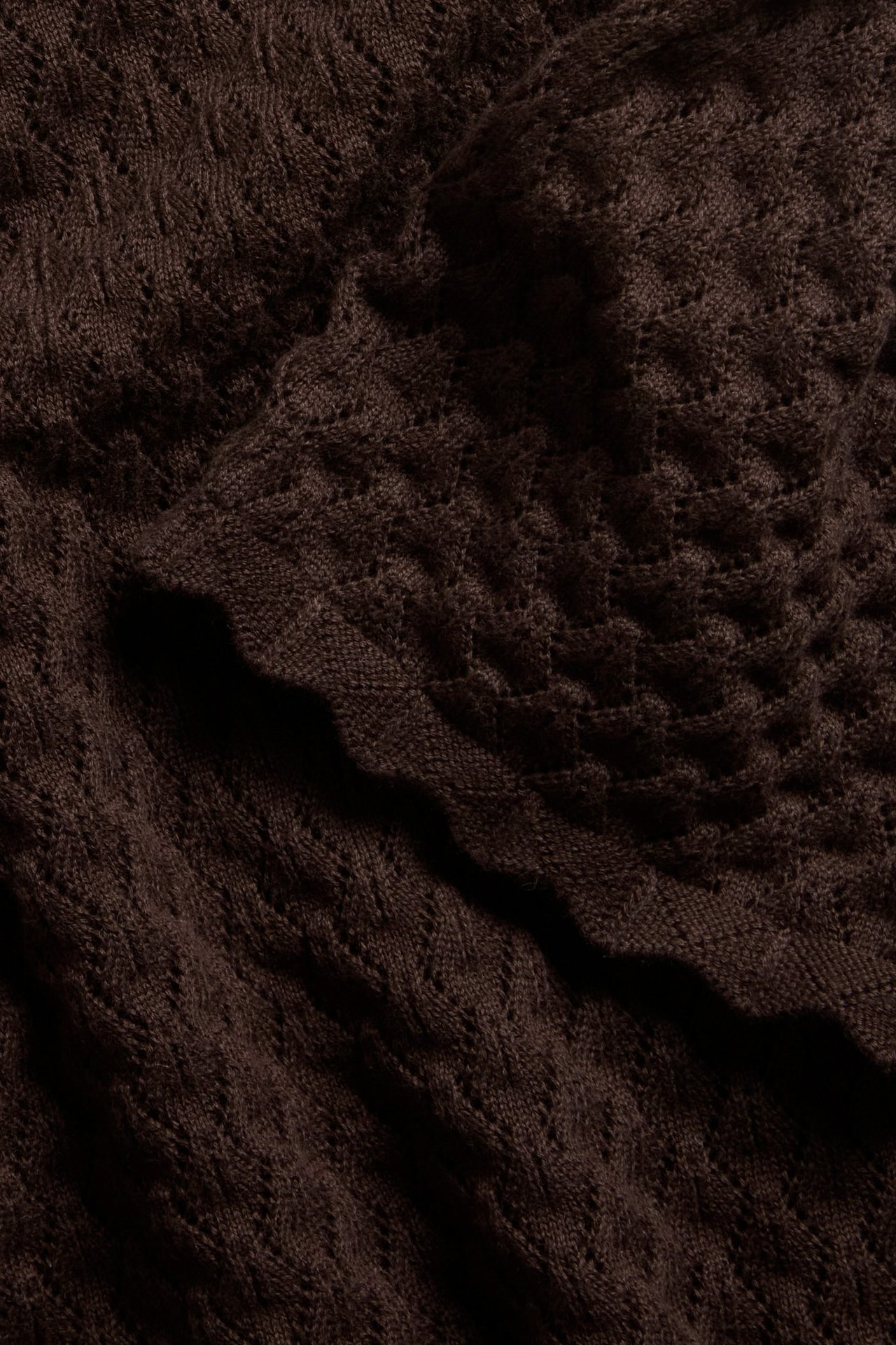 Zbliżenie na ciemnobrązowy, wzorzysty bawełniany sweter z krótkim rękawem, z ażurowym splotem i falistym brzegiem.