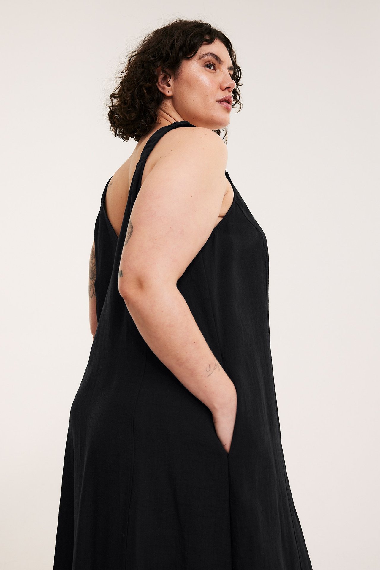 Sidovy av en kvinna i en löst sittande, lång svart klänning i viskosmix med V-ringning och fickor.