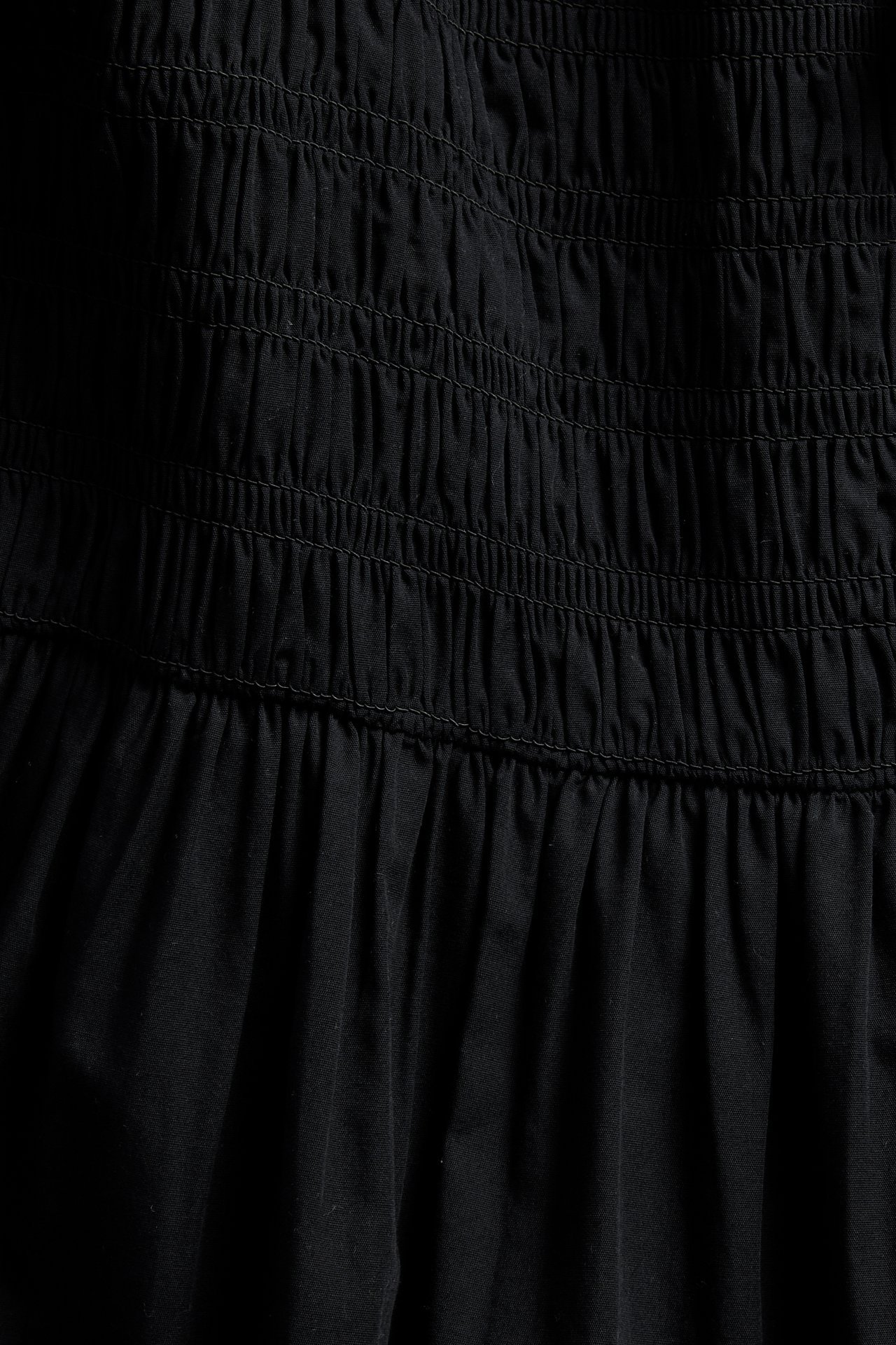 Zbliżenie na czarną bawełnianą sukienkę popelinową z poziomym marszczeniem i rozkloszowaną spódnicą.