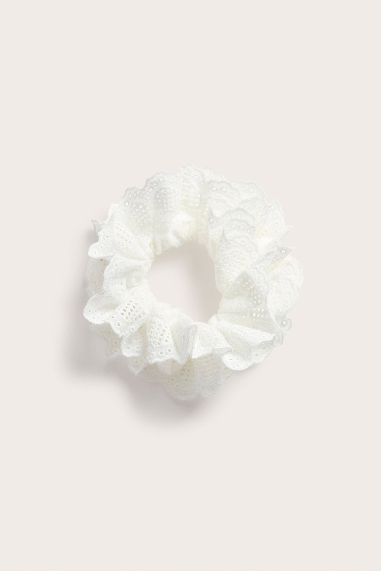 Toppvy av en offwhite scrunchie med volang och broderie anglaise-mönster.