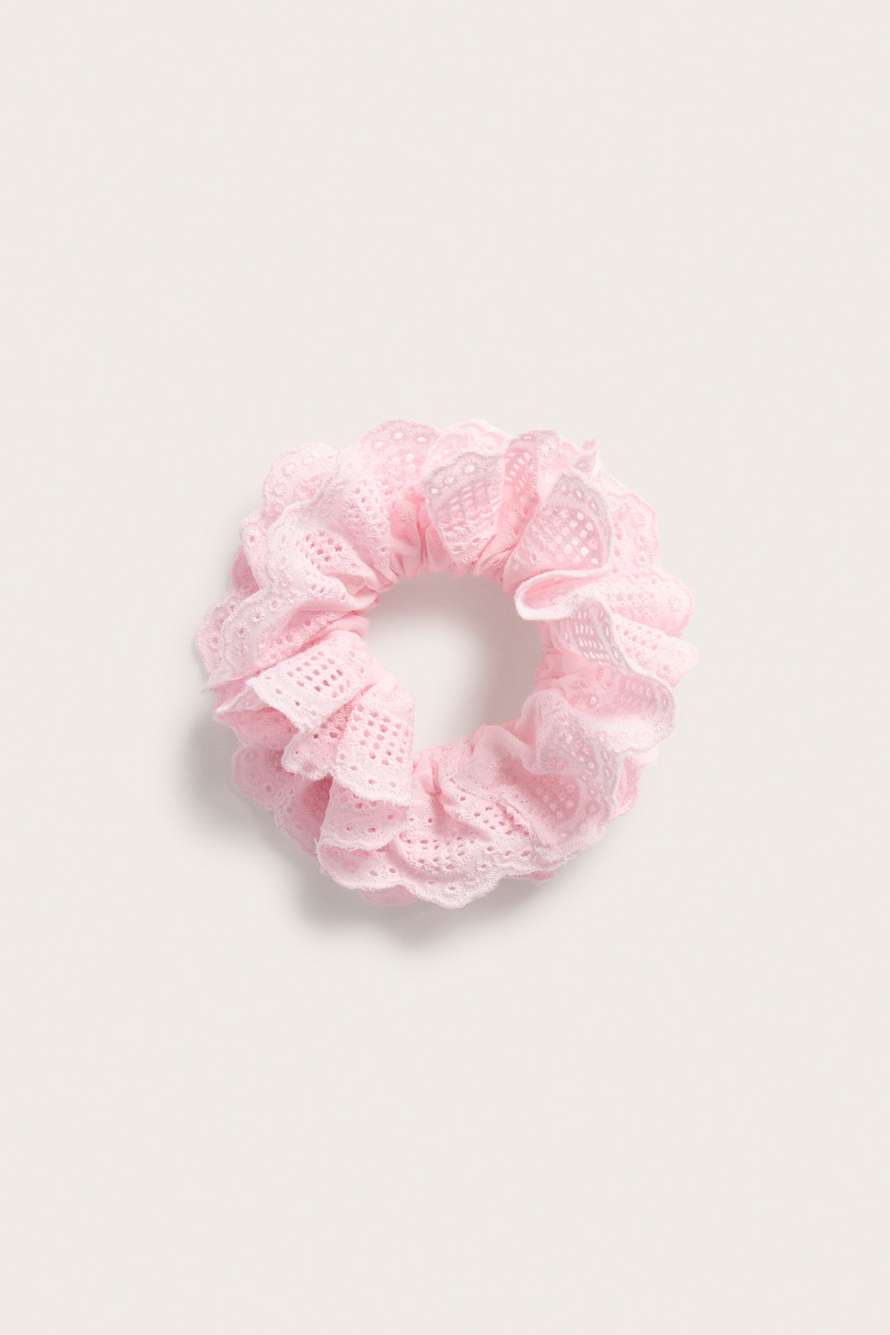 Närbild av en volangprydd rosa scrunchie med broderie anglaise-mönster.
