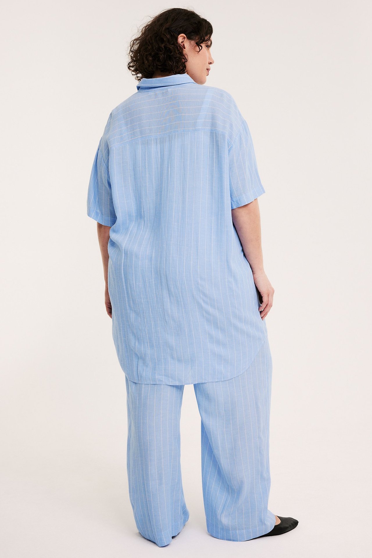 Ryggvy av kvinna i ljusblå randig kortärmad långskjorta och matchande byxor.