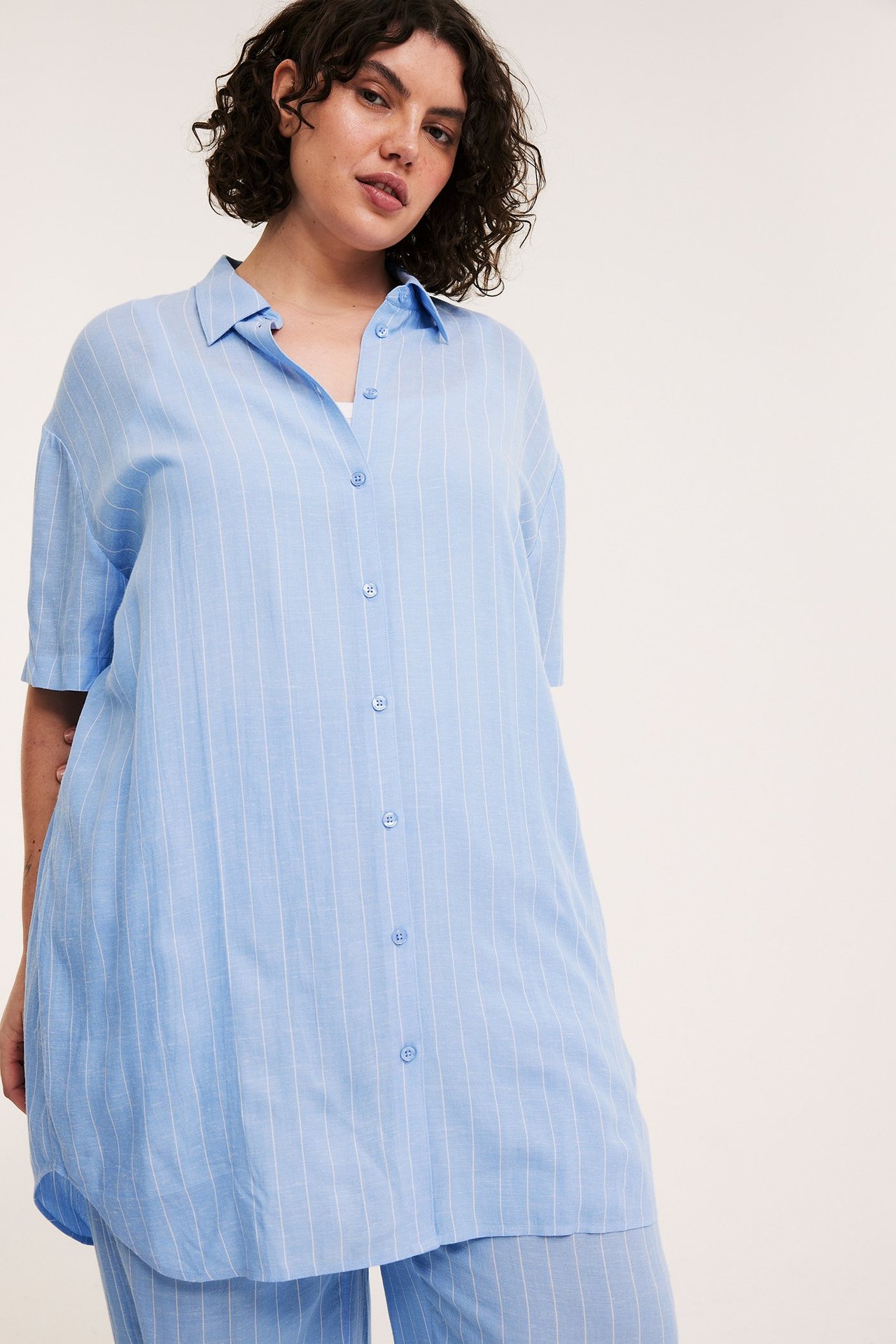 Frontvy av kvinna i en avslappnad ljusblå randig långskjorta i viskosmix och matchande byxor.