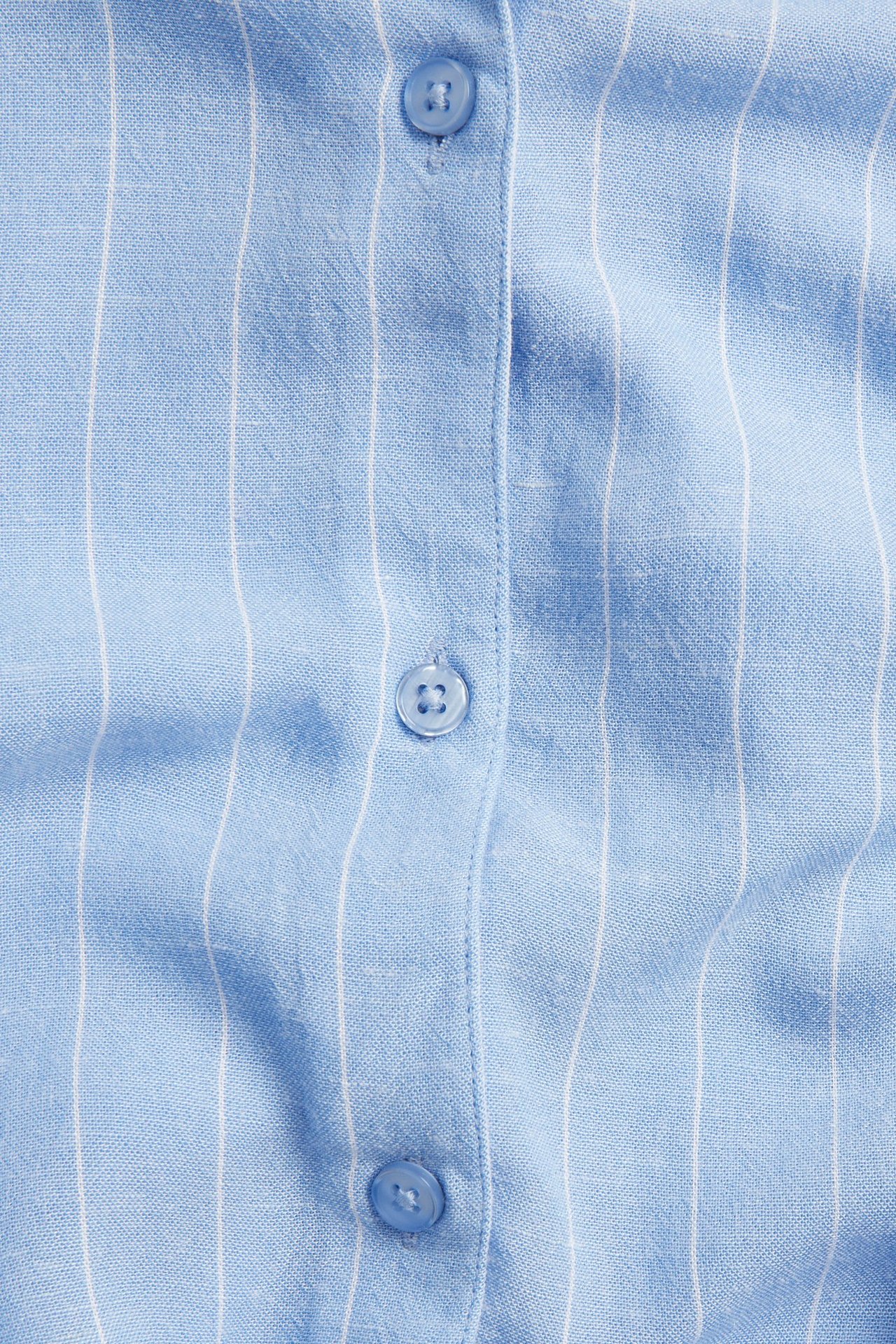 Närbild av en ljusblå- och vitrandig långskjorta i viskosmix med blå knappar.