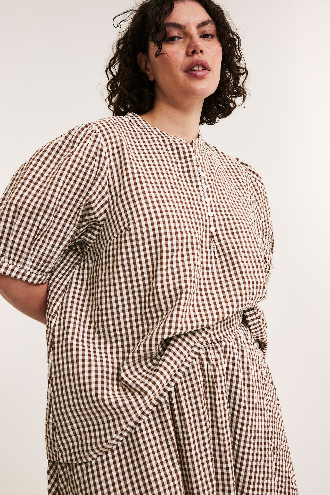 Edestä, nainen yllään ruskearuudullinen seersucker-pusero, jossa pussihihat ja pyöreä pääntie.