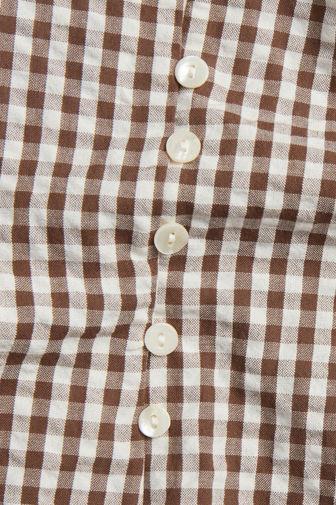 Lähikuva ruskeavalkoisesta ruudullisesta ryppykangas-puserosta, jossa rivi valkoisia nappeja.