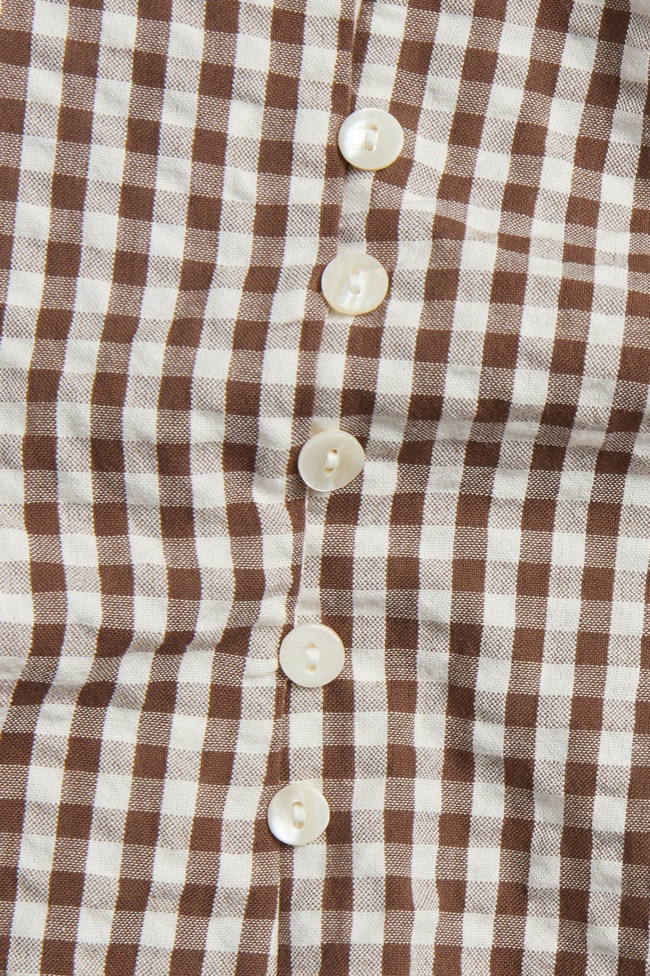 Zbliżenie brązowo-białej bluzki z krepy w kratkę z rzędem białych guzików.