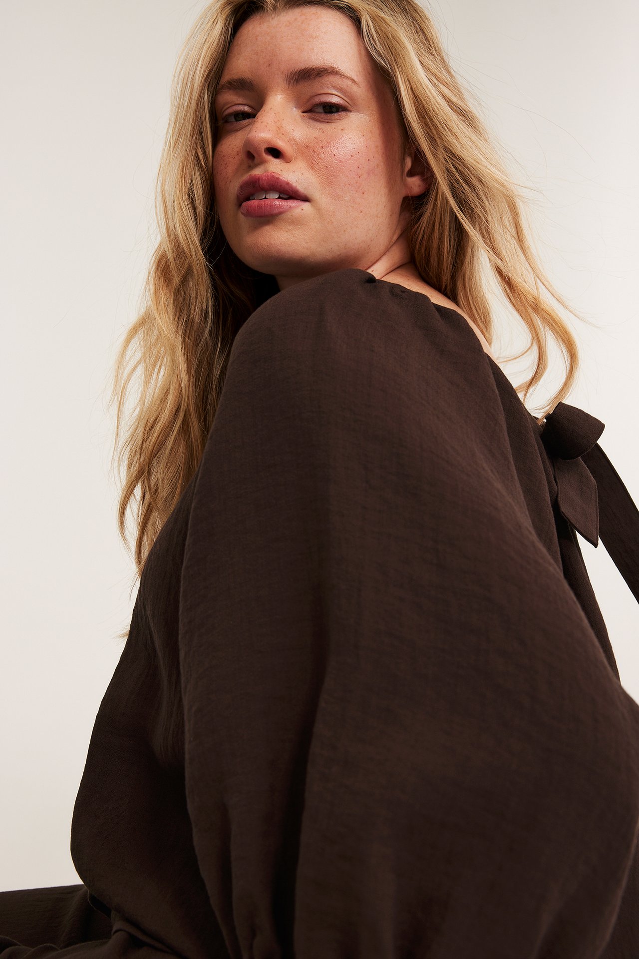 Närbild på en kvinna i en mörkbrun singoallablus i viskosmix med kort puffärm och knytdetalj.