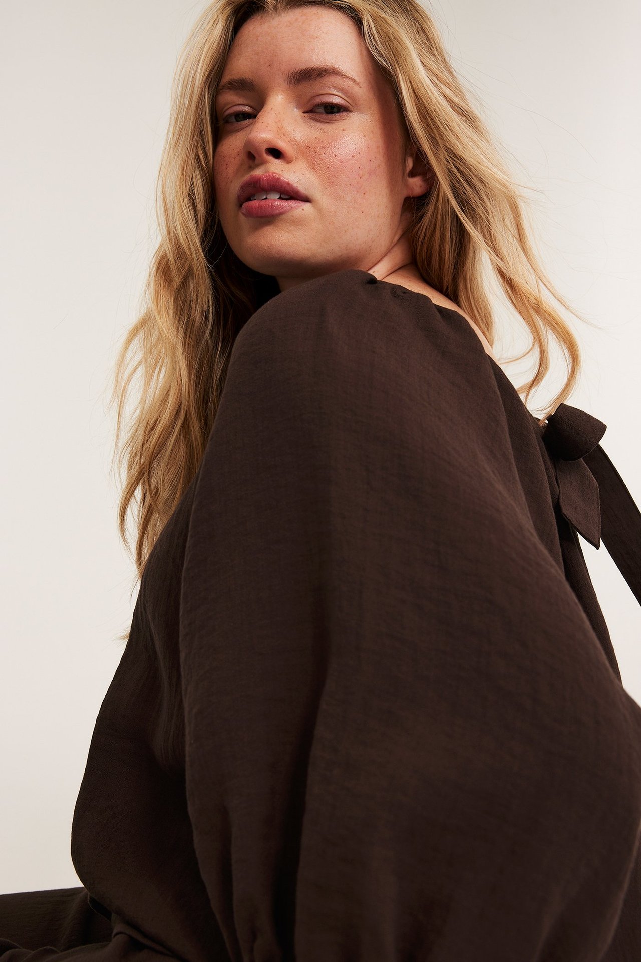 Lähikuva naisesta tummanruskeassa viskoosisekoitteisessa Singoalla-puserossa, jossa puffihihat ja solmuyksityiskohta.