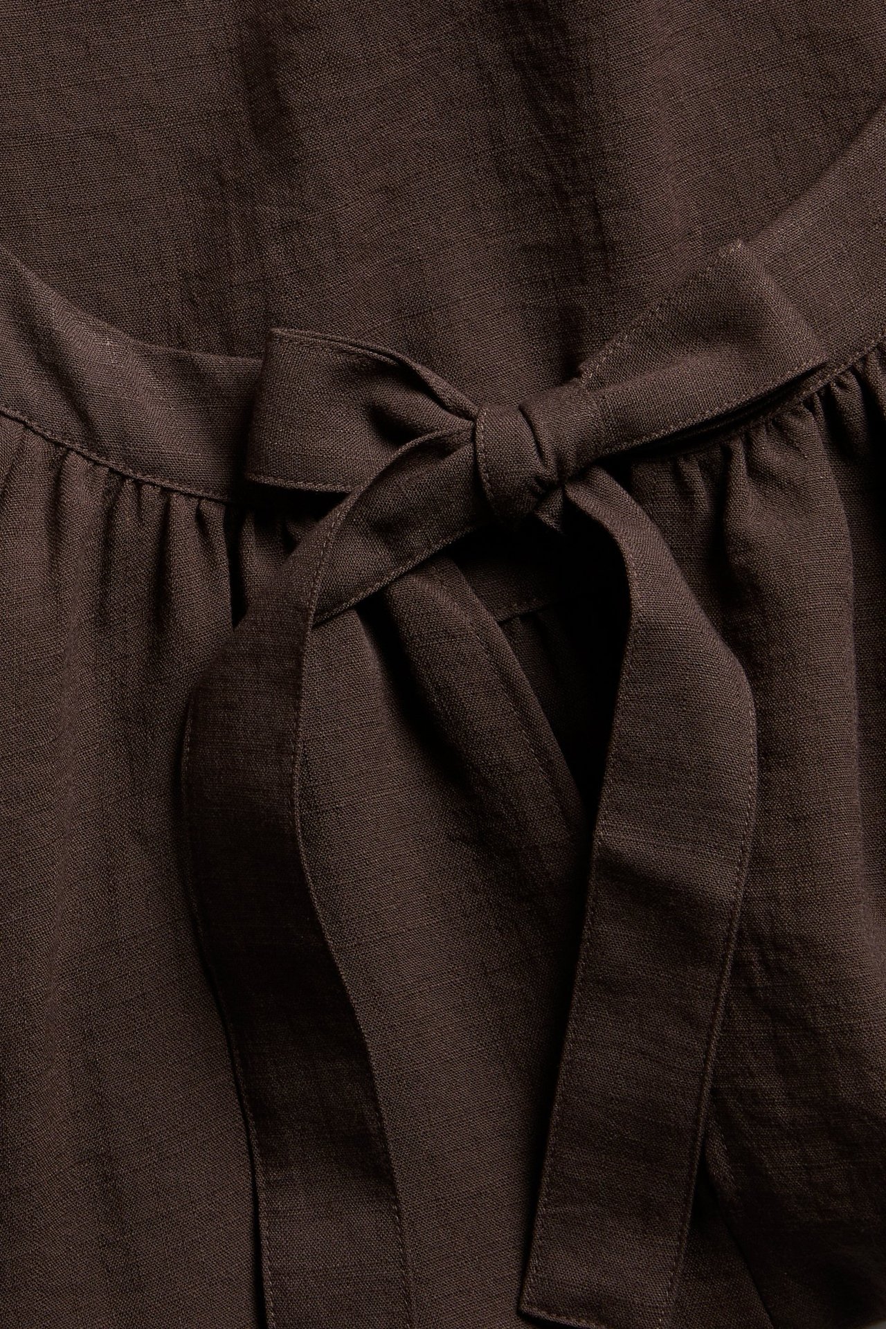 Närbild på en mörkbrun Singoallablus i viskosmix med knuten rosett och rynkad detalj.