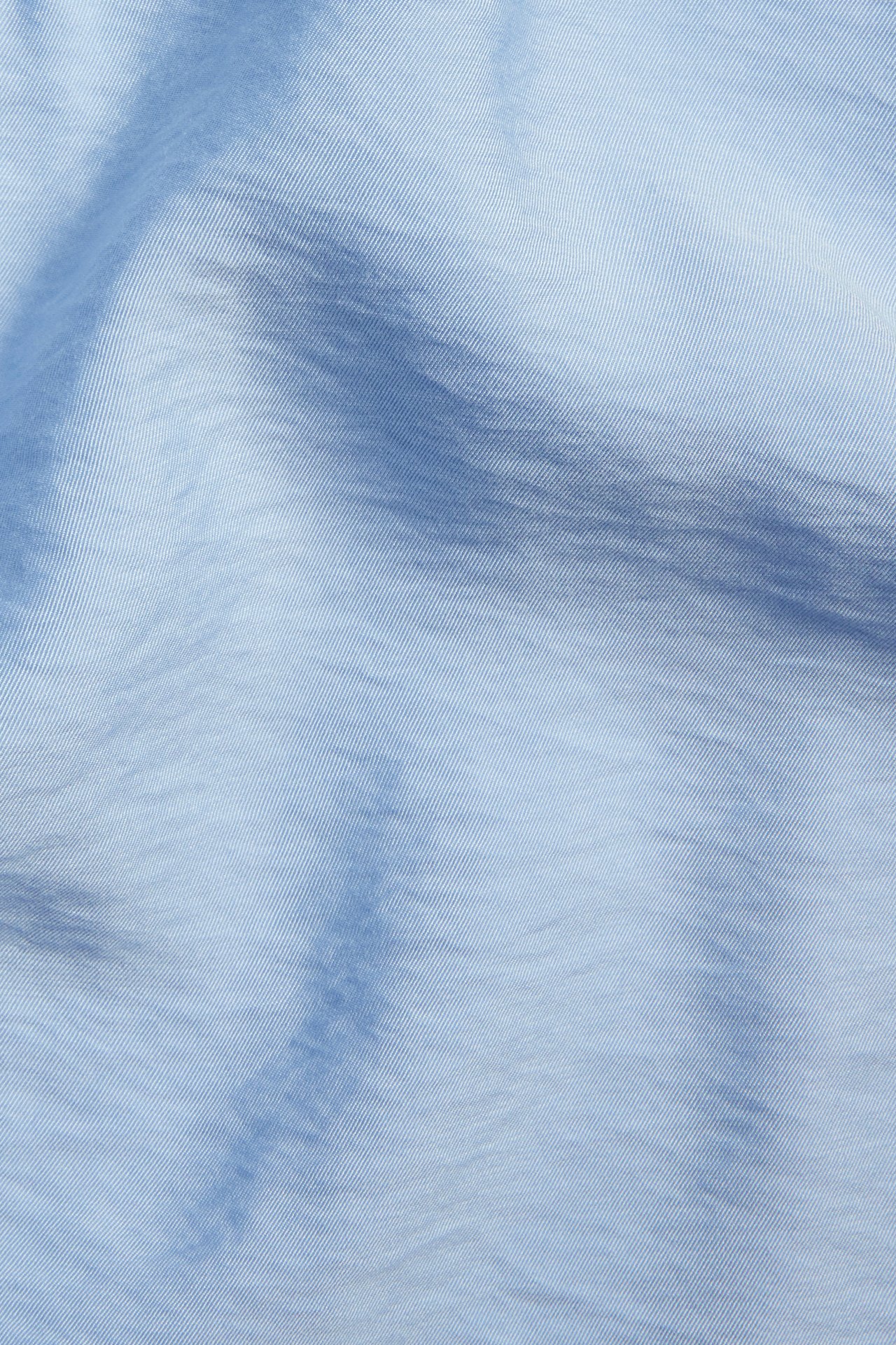 Zbliżenie jasnoniebieskiego, jednolitego materiału koszuli popover, ukazujące subtelny splot diagonalny i zagniecenia.