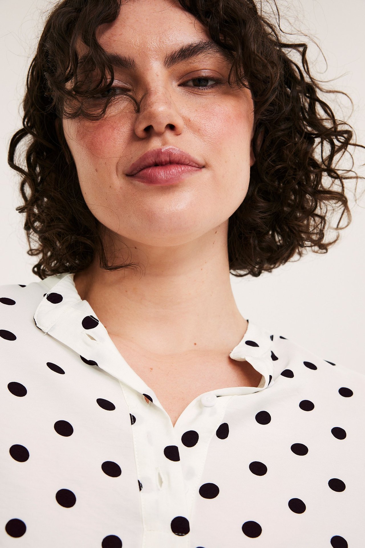 Zbliżenie z przodu: Kobieta w luźnej, écru bluzce popover w kropki, z dekoltem V bez kołnierza.