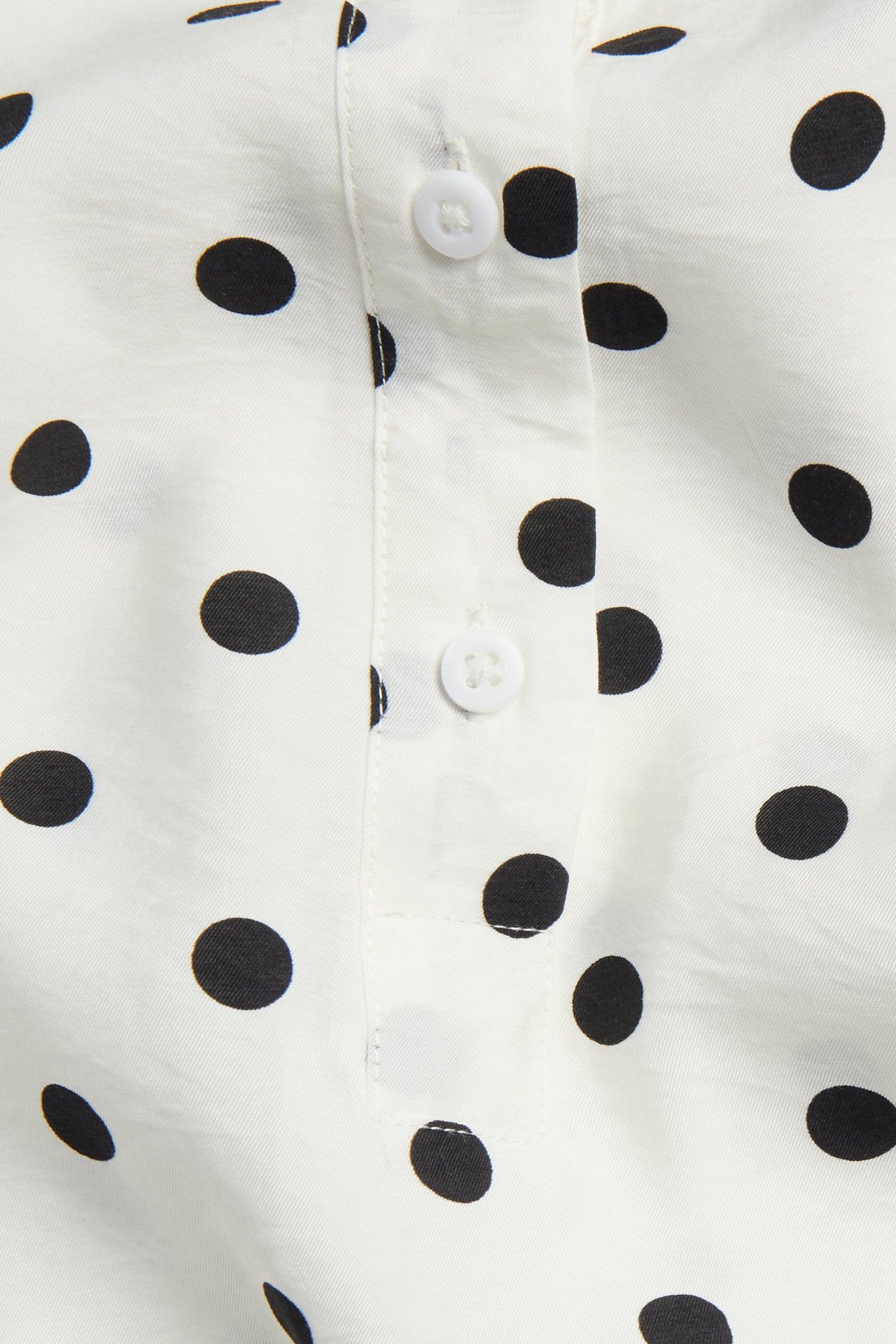 Närbild av en offwhite prickig popover blus med kort vit knappslå.