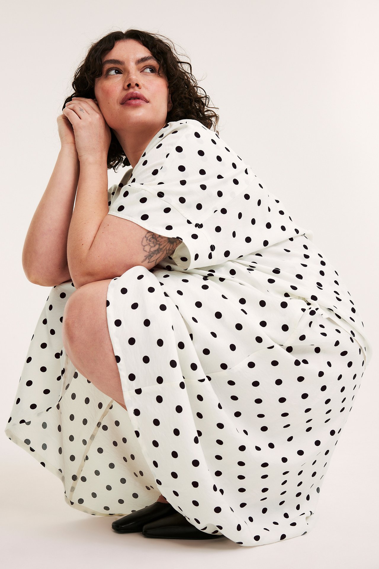 Widok z przodu: Kucająca kobieta w luźnej ecru bluzce popover w kropki i czarnych butach.