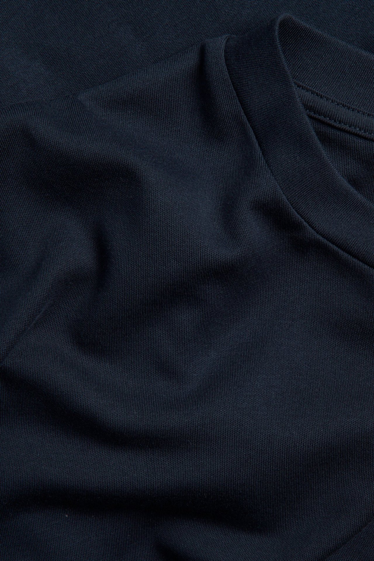 Zbliżenie ciemnoniebieskiego, jednolitego, obszernego t-shirtu z bawełny interlock, pokazujące dekolt.