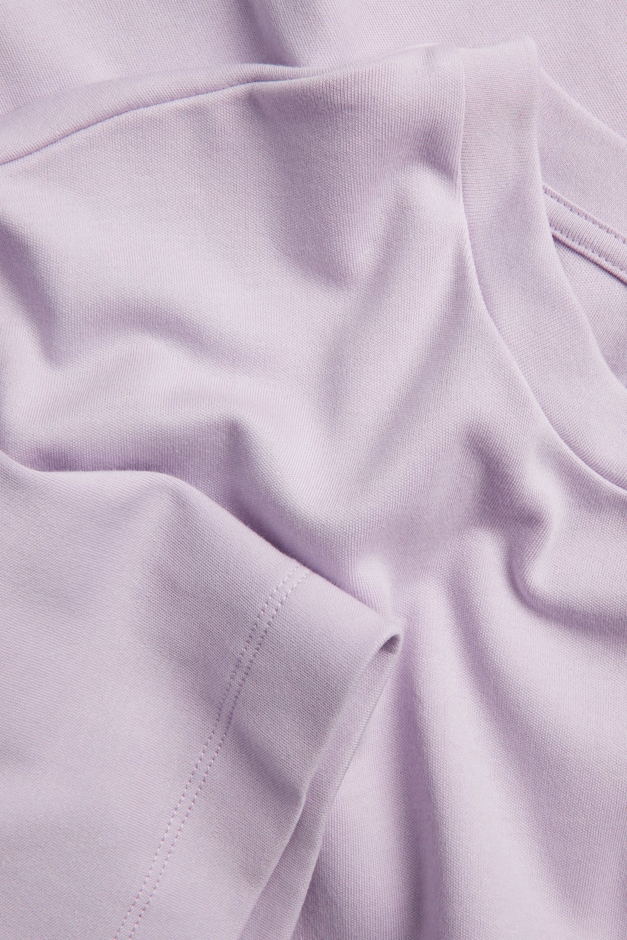 Zbliżenie na oversizowy jasnofioletowy t-shirt z bawełnianego interlocku, widoczny rękaw i kołnierz.