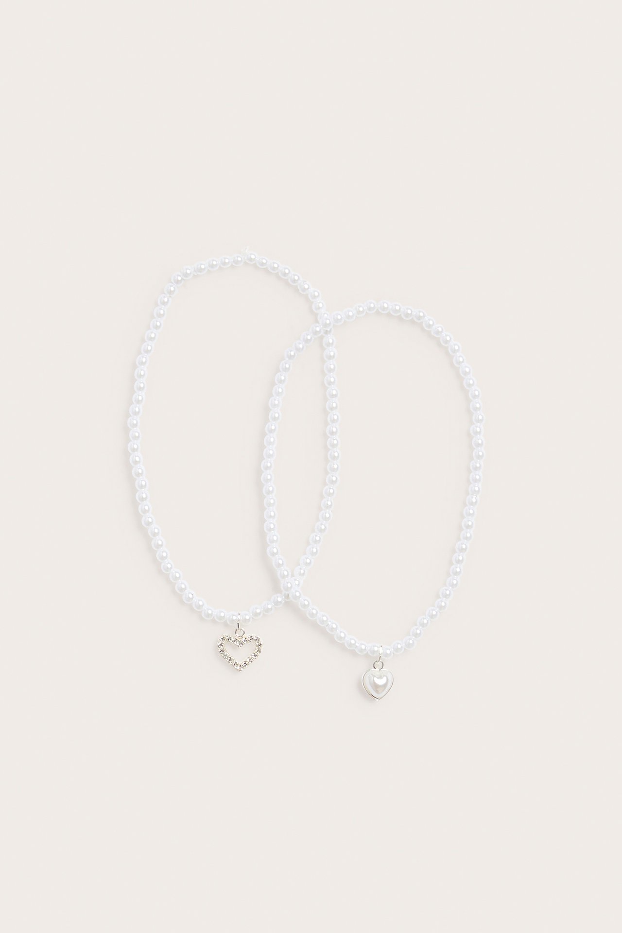 Uppifrån: Två offwhite pärlhalsband, ett med glitterhjärta, det andra med ett enkelt hjärthänge.