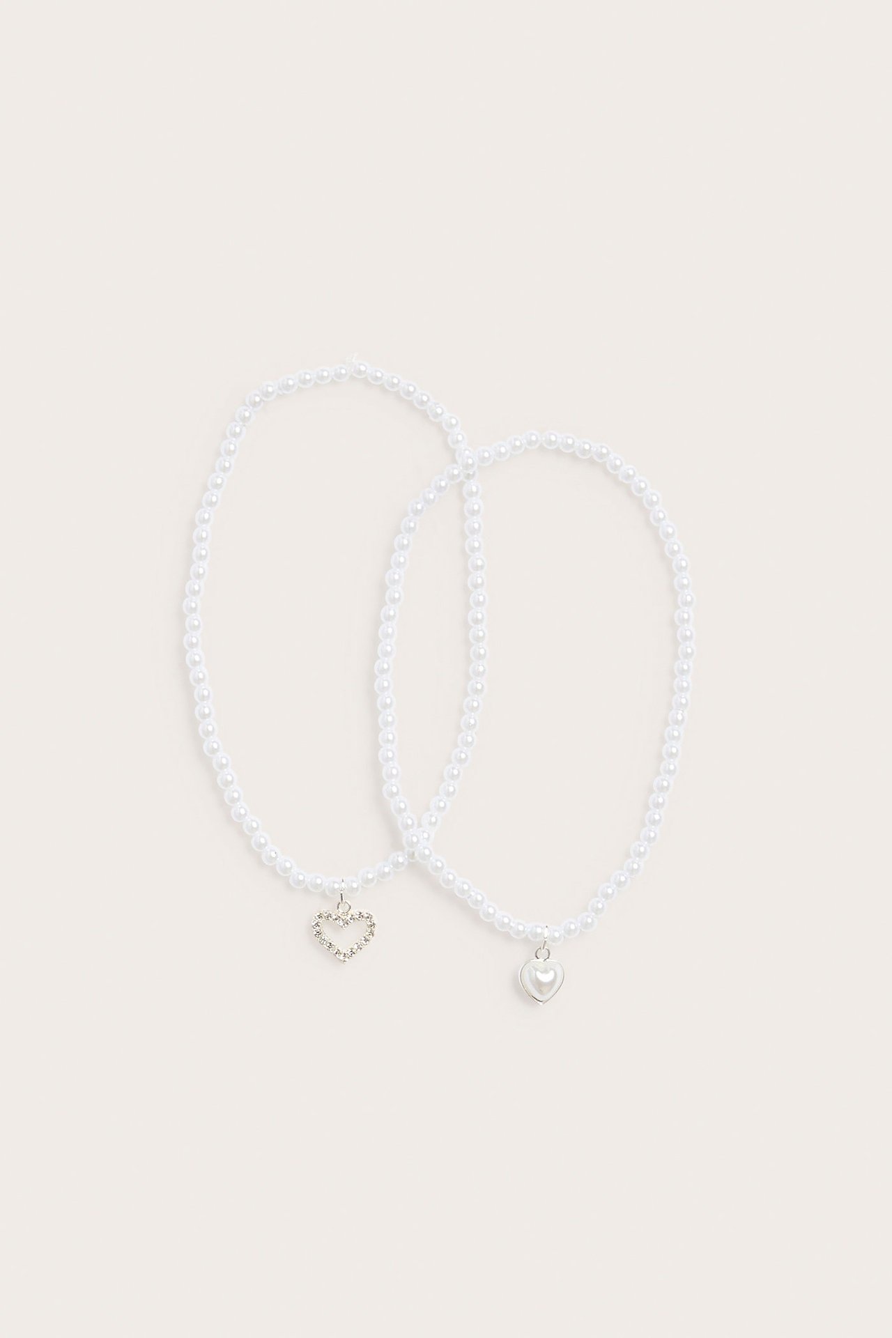 Ylhäältä: Kaksi luonnonvalkoista helmikaulakorua, toisessa glitter sydänriipus, toisessa pelkkä sydän.