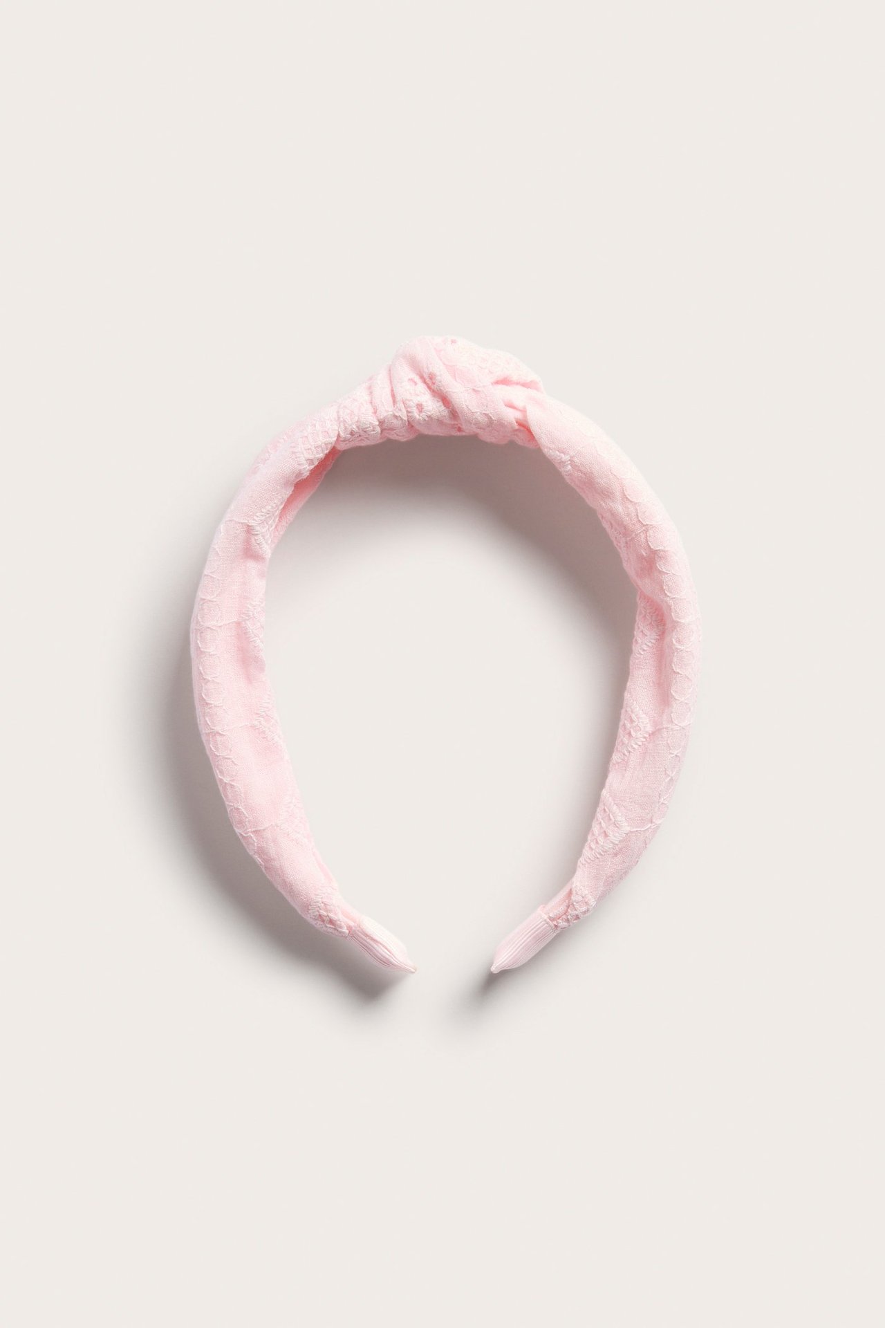 Närbild uppifrån på ett rosa tygdiadem med broderie anglaise och en knuten detalj.