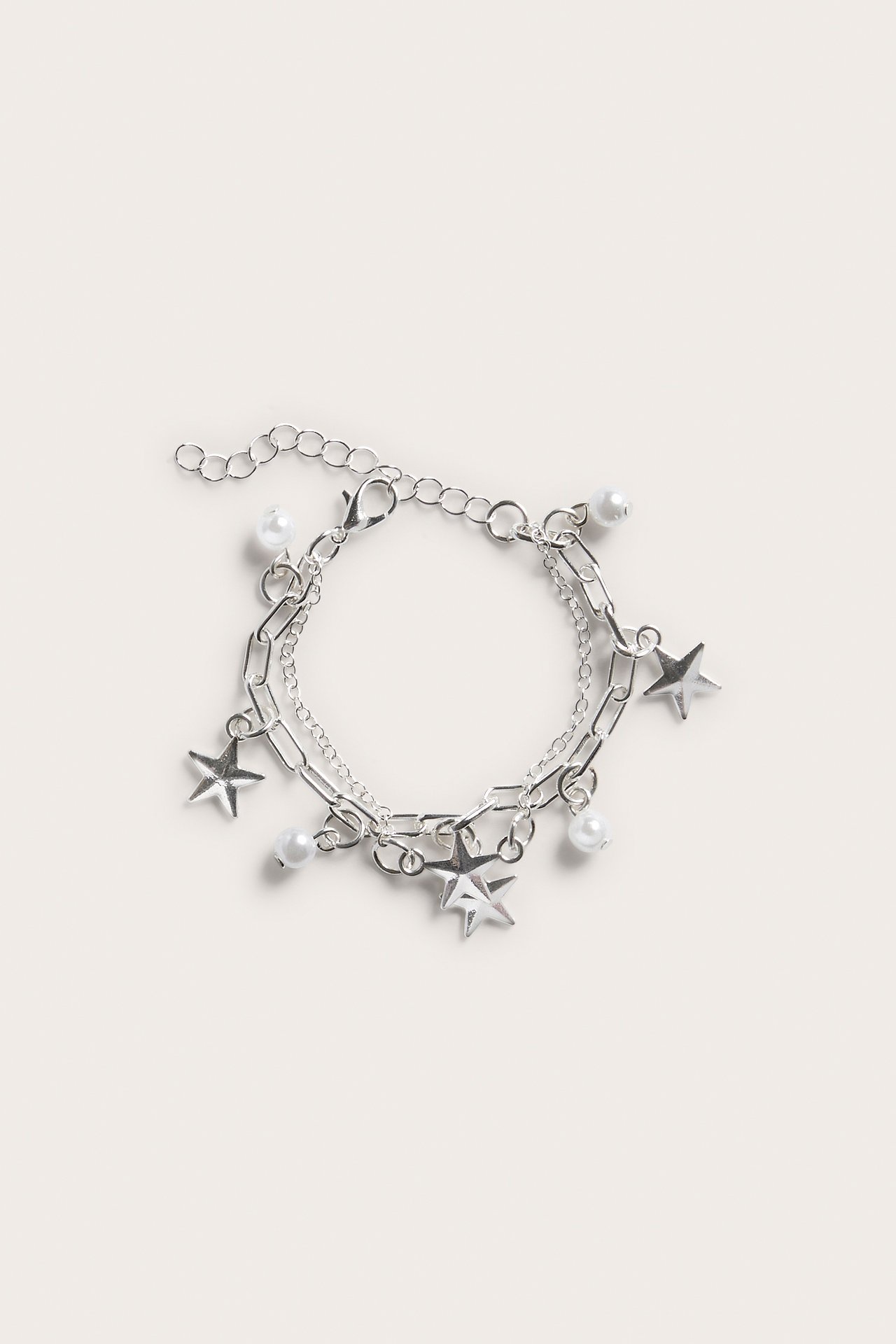 Överblick av ett silverfärgat tvåradigt armband med pärl- och stjärnberlocker, med ett karbinlås.
