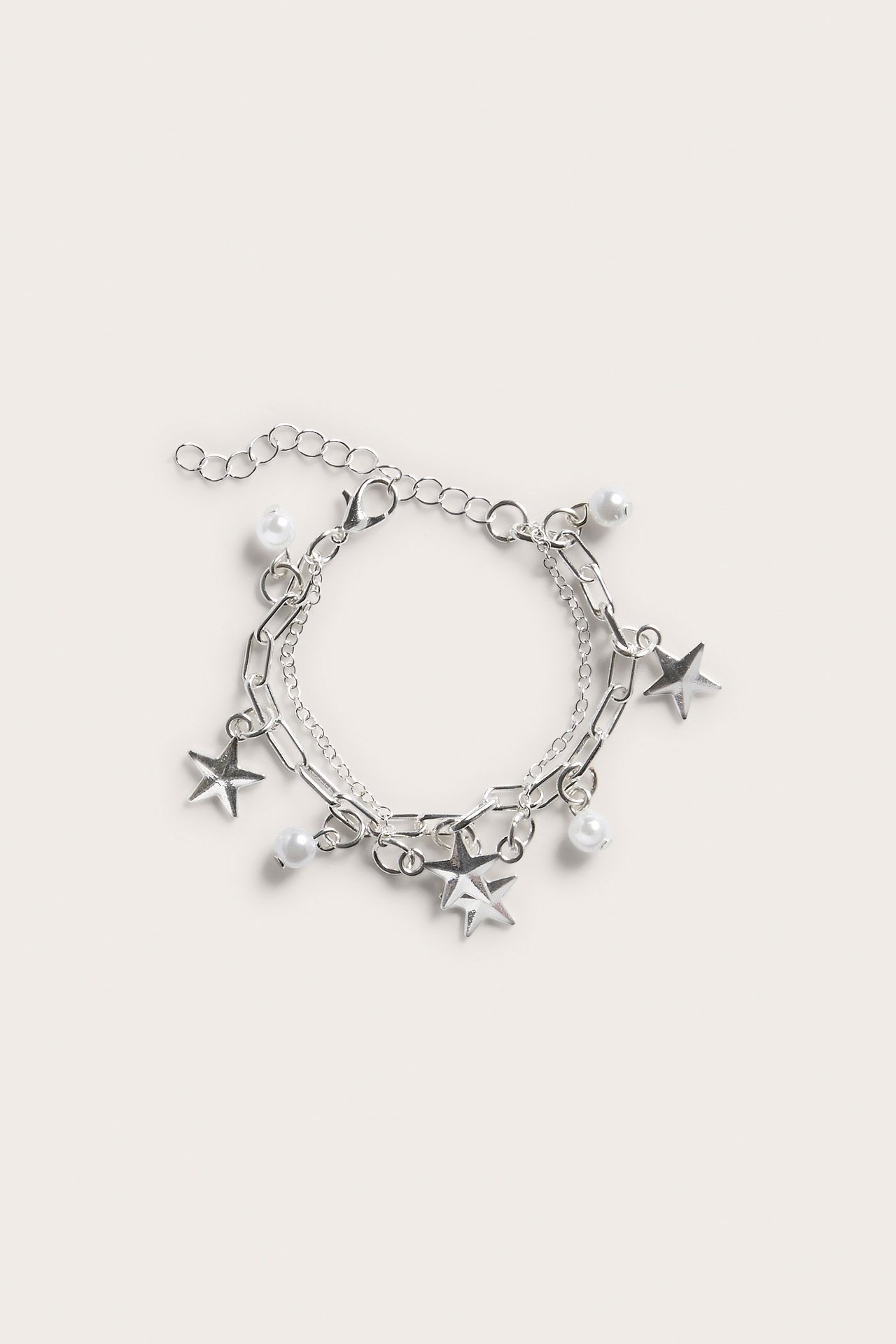 Yleiskuva hopeisesta kaksirivisestä rannekorusta, jossa helmi- ja tähtiriipuksia, ja papukaijalukko.